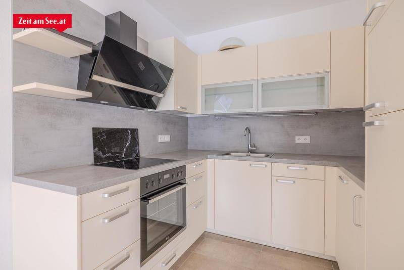 Moderne Einbauküche mit beigen Schränken, Induktionskochfeld, Backofen und Dunstabzugshaube.