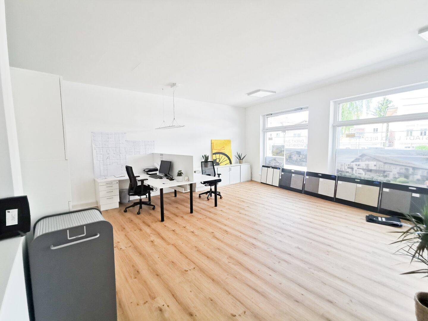 Geräumiges Büro mit großen Fenstern, hellem Holzboden und minimalistischer Einrichtung.