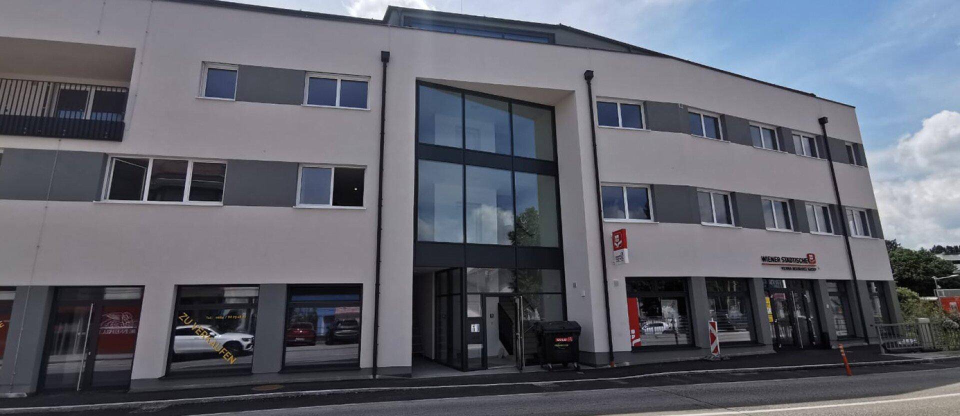Moderne Gebäudefassade mit großzügigem Glaseingangsbereich und Geschäftsflächen im Erdgeschoss.