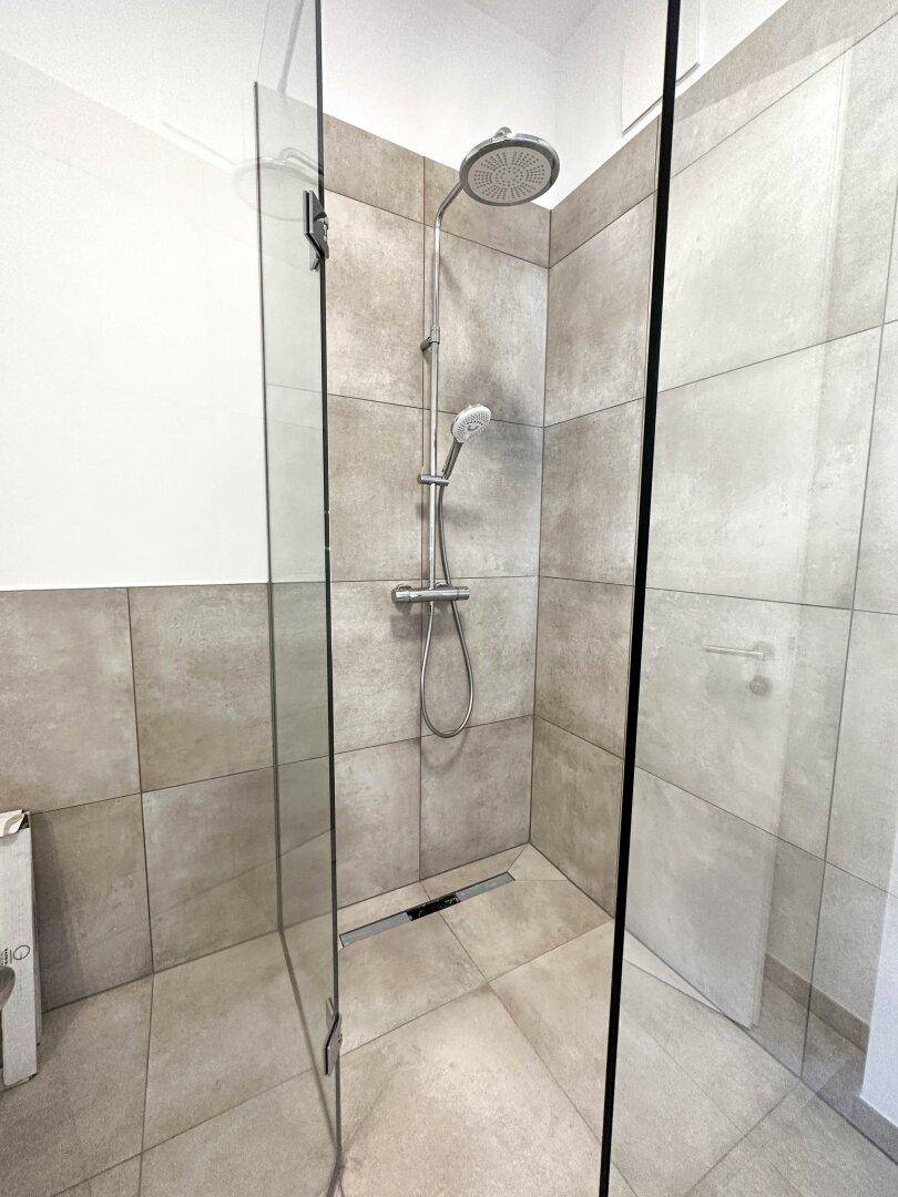Geräumige, moderne begehbare Dusche mit Regenduschkopf und großen Fliesen.