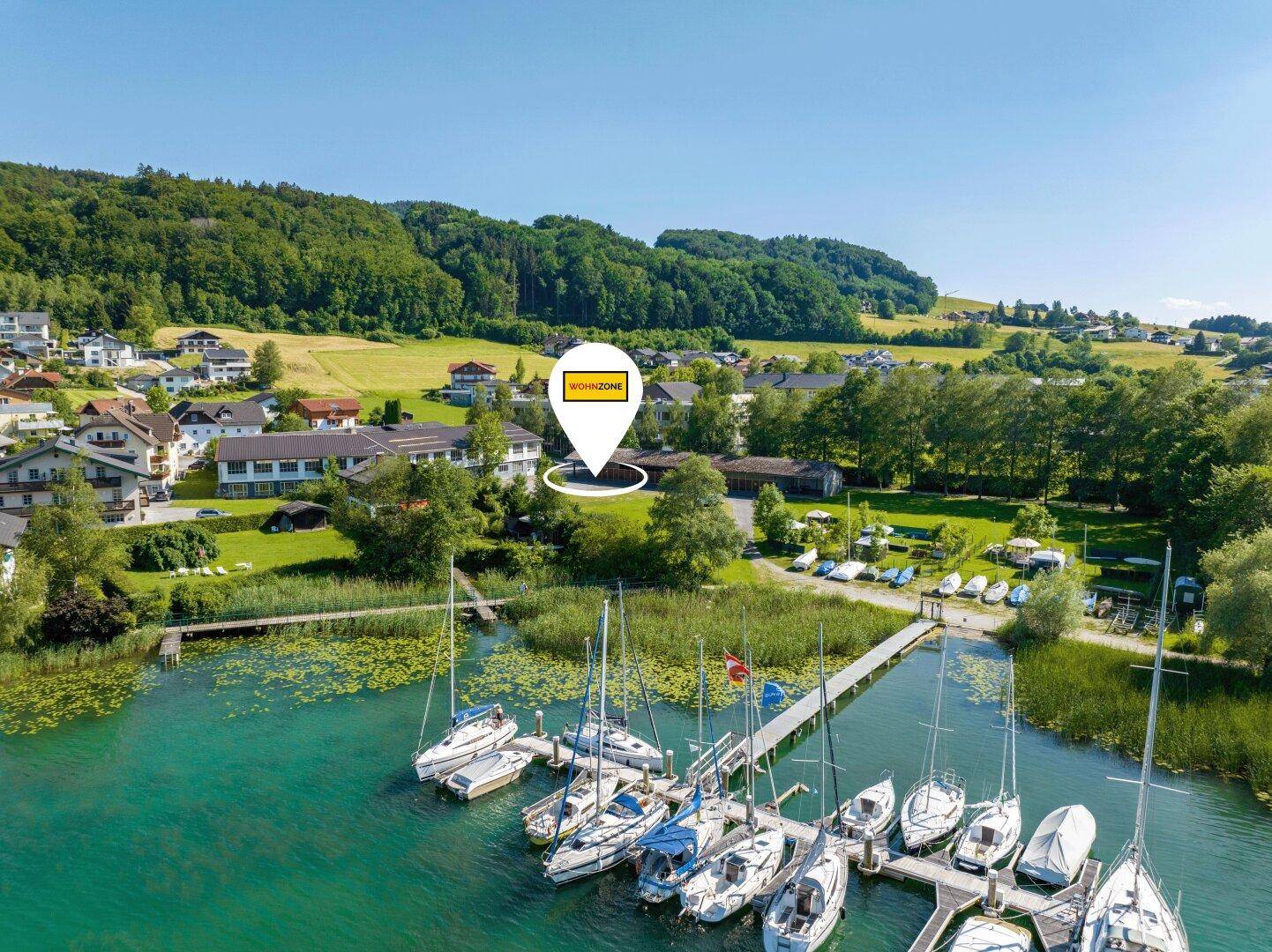 Luftaufnahme eines malerischen Sees mit Segelbooten und umliegender grüner Landschaft.