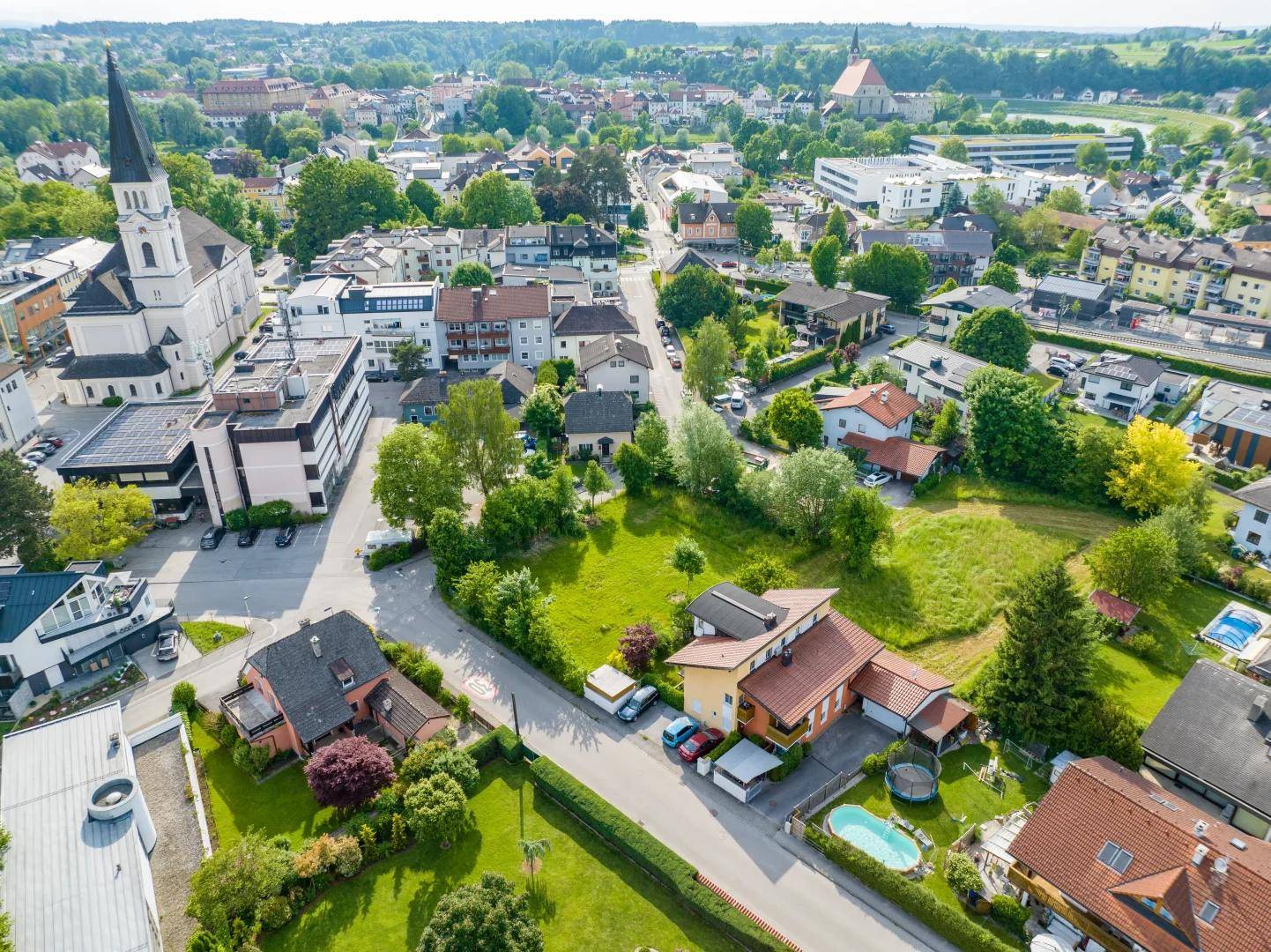 Luftaufnahme einer grünen Wohngegend mit Einfamilienhäusern, Gärten und einem Kirchturm.