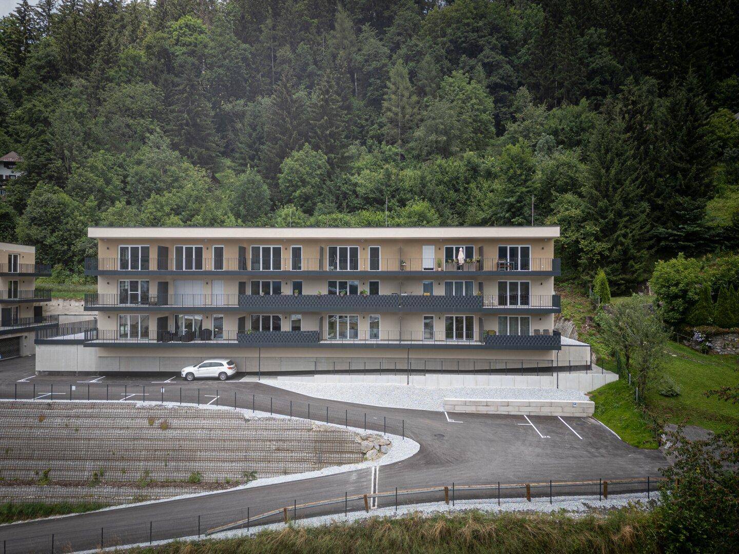 Modernes Mehrfamilienhaus in grüner Hanglage mit Balkonen und Tiefgaragenzufahrt.