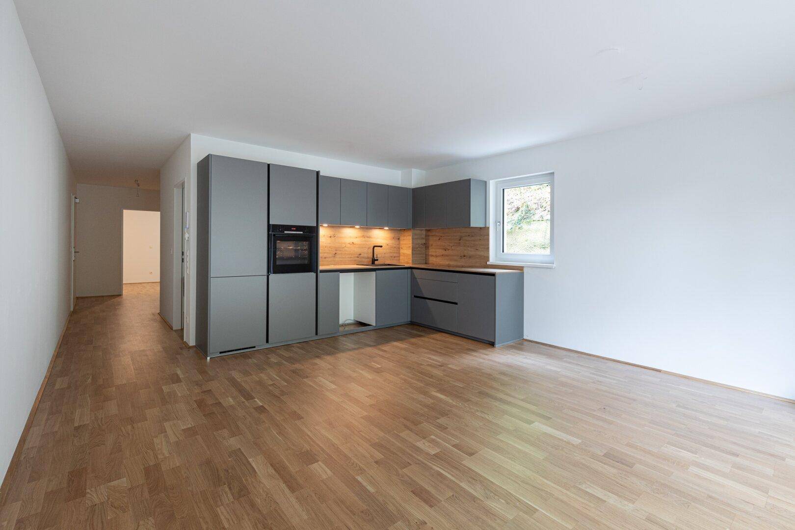 Helle, offene Küche mit grauen Schränken, Holzakzenten und Parkettboden in einem Neubau.