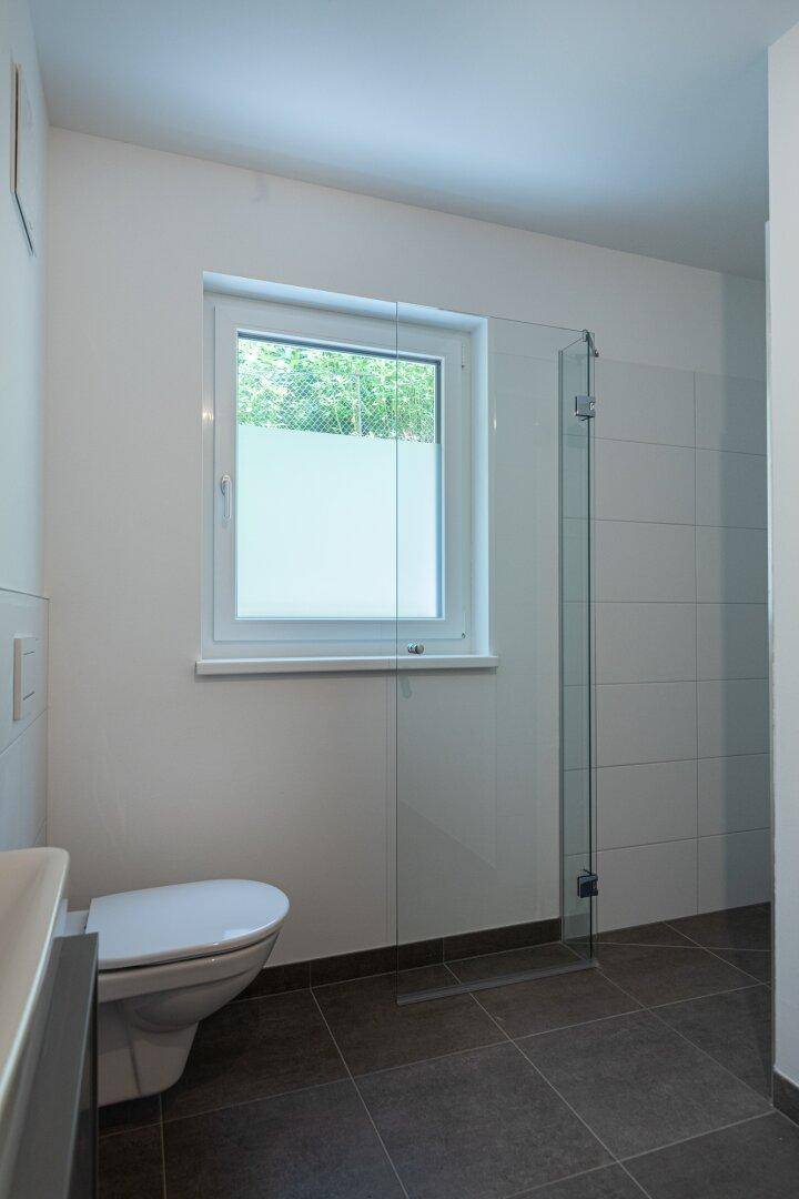Modernes Badezimmer mit bodengleicher Dusche, Wand-WC und Fenster für Tageslicht.