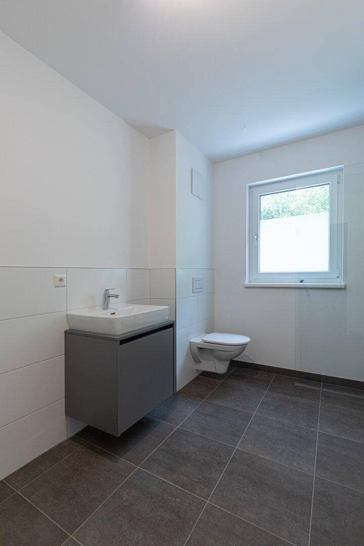 Modernes Badezimmer mit schwebendem Waschtisch, Wand-WC und großformatigen Fliesen.