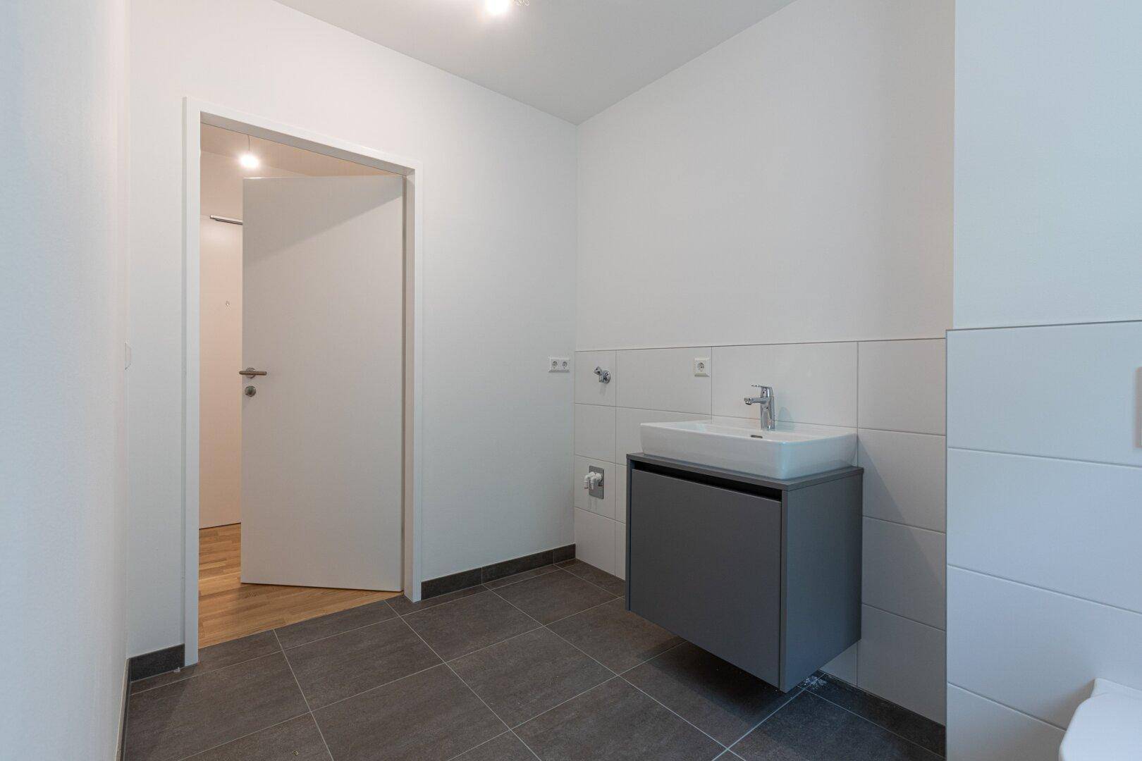 Helles Badezimmer mit modernem Waschtisch und Fliesenboden, Blick zum Flur.