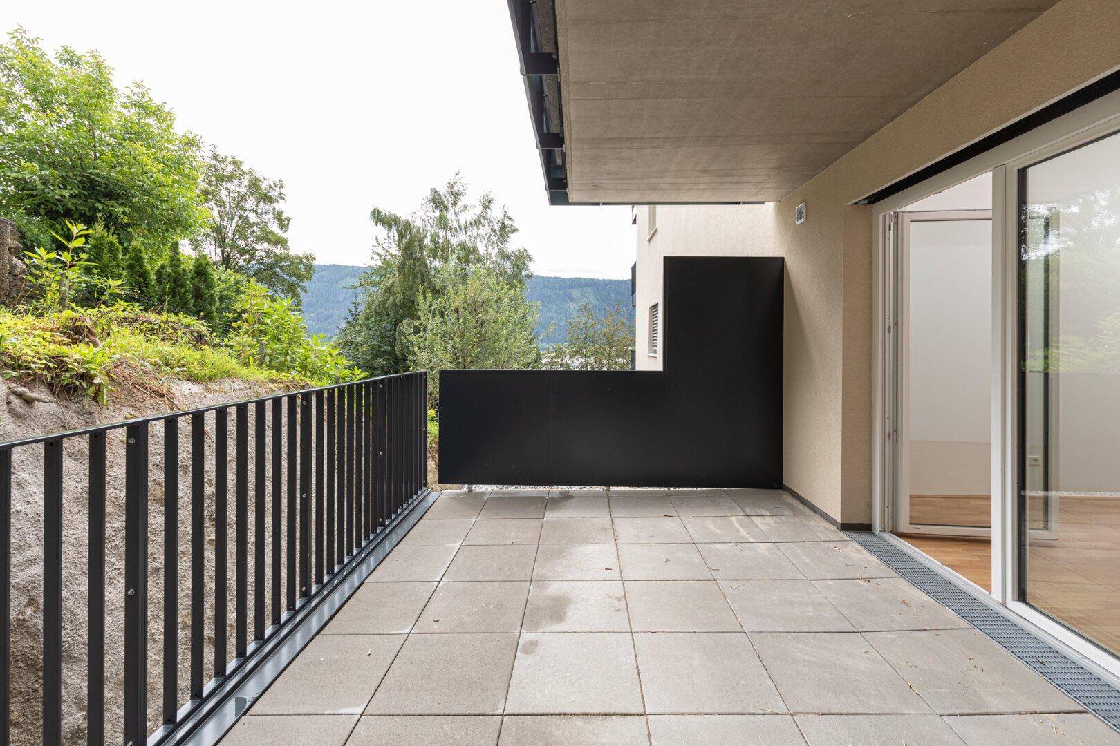 Geräumiger Balkon mit Fliesenboden, schwarzem Geländer und weitem Blick auf die Berge und Natur.