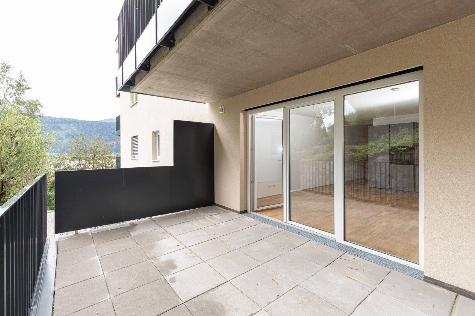 Heller Balkon mit großen Schiebetüren, Fliesenboden und Ausblick ins Grüne.