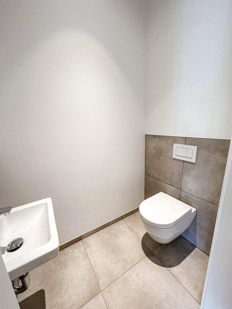 Kompaktes Gäste-WC mit wandhängender Toilette und kleinem Waschbecken auf Fliesenboden.