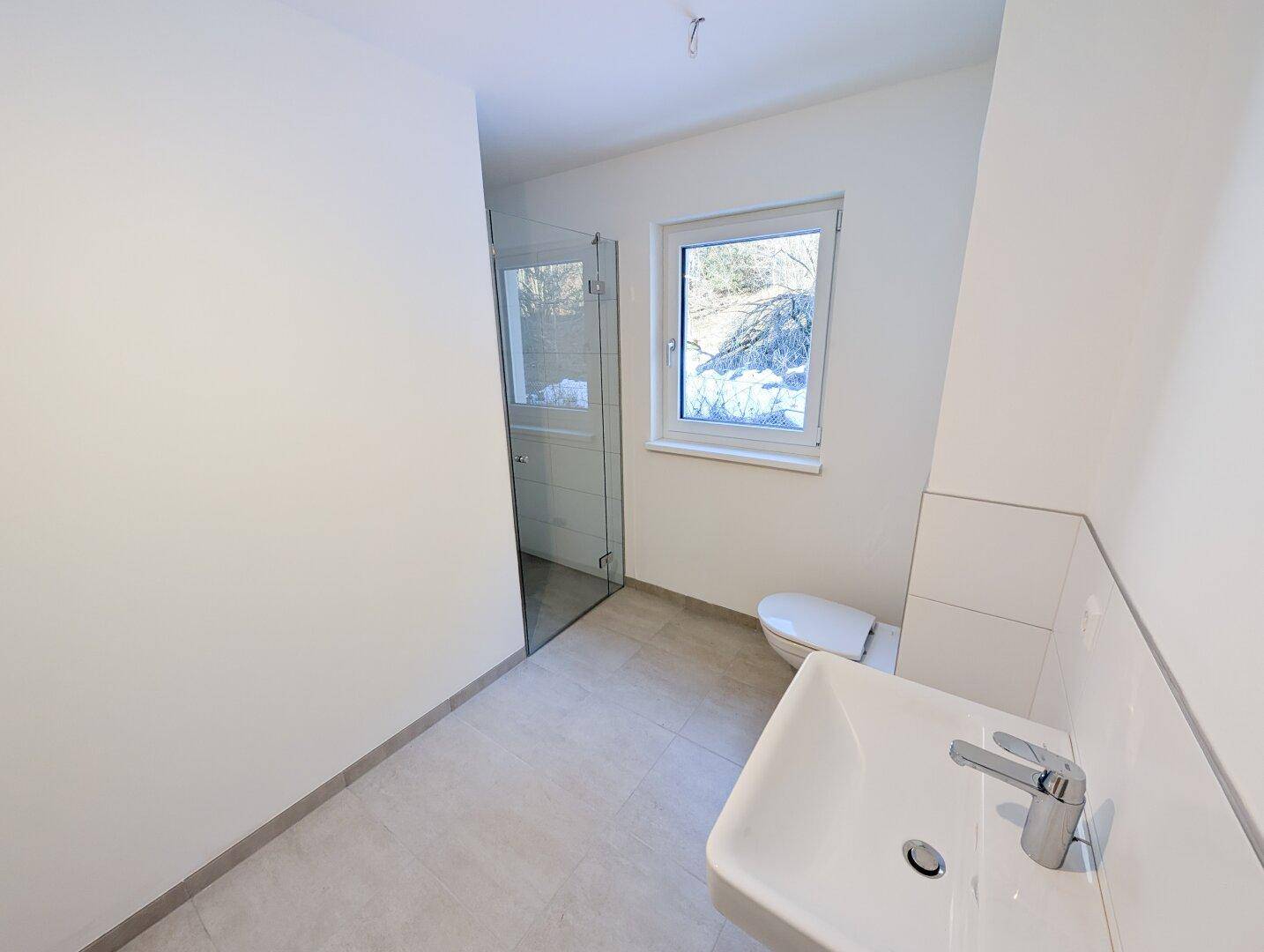Modernes Badezimmer in neuwertigem Zustand mit ebenerdiger Dusche, Waschbecken und Fenster für Tageslicht.