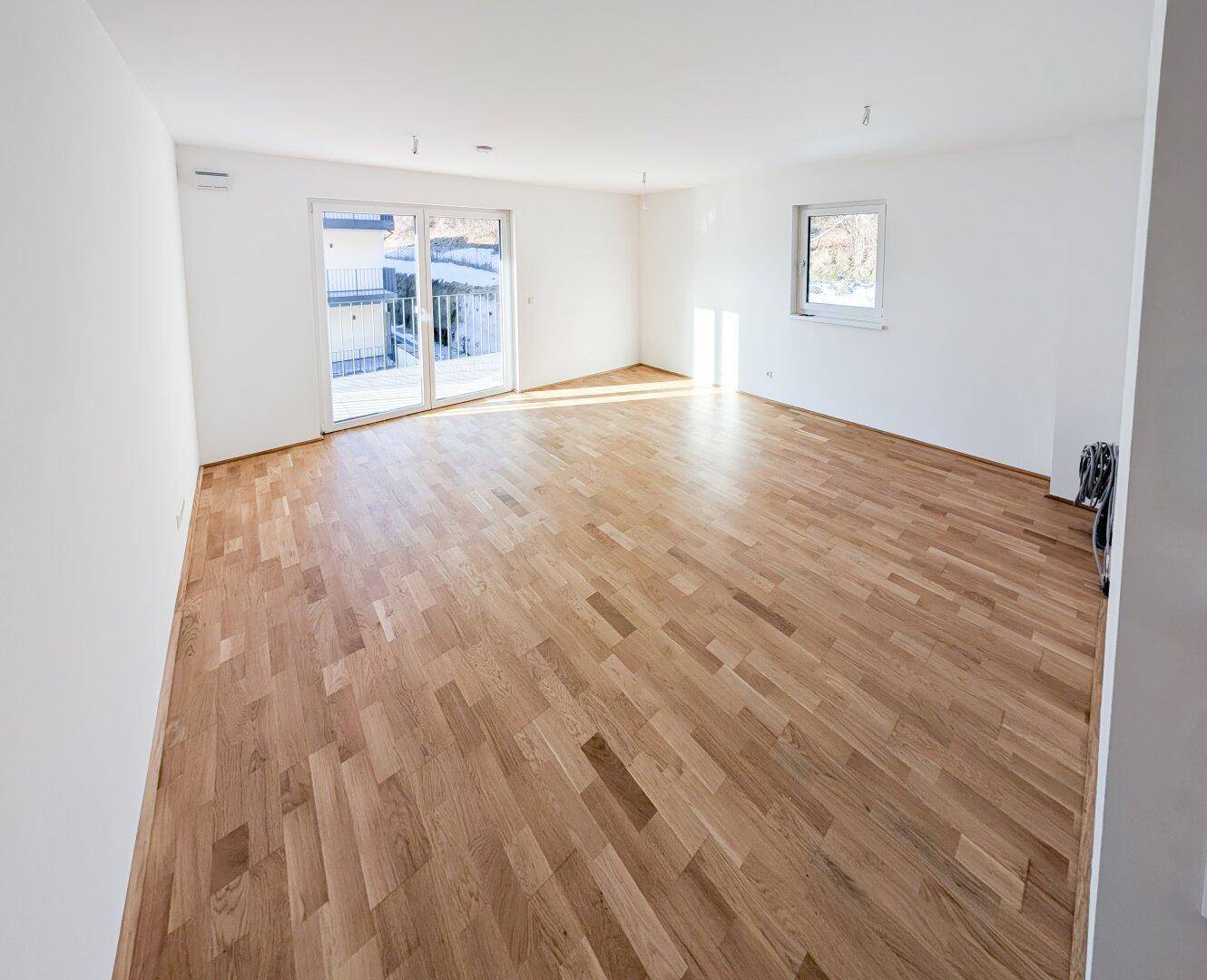 Heller, leerer Wohnraum mit neuem Parkettboden und Zugang zu einem Balkon, ideal für individuelle Gestaltung.