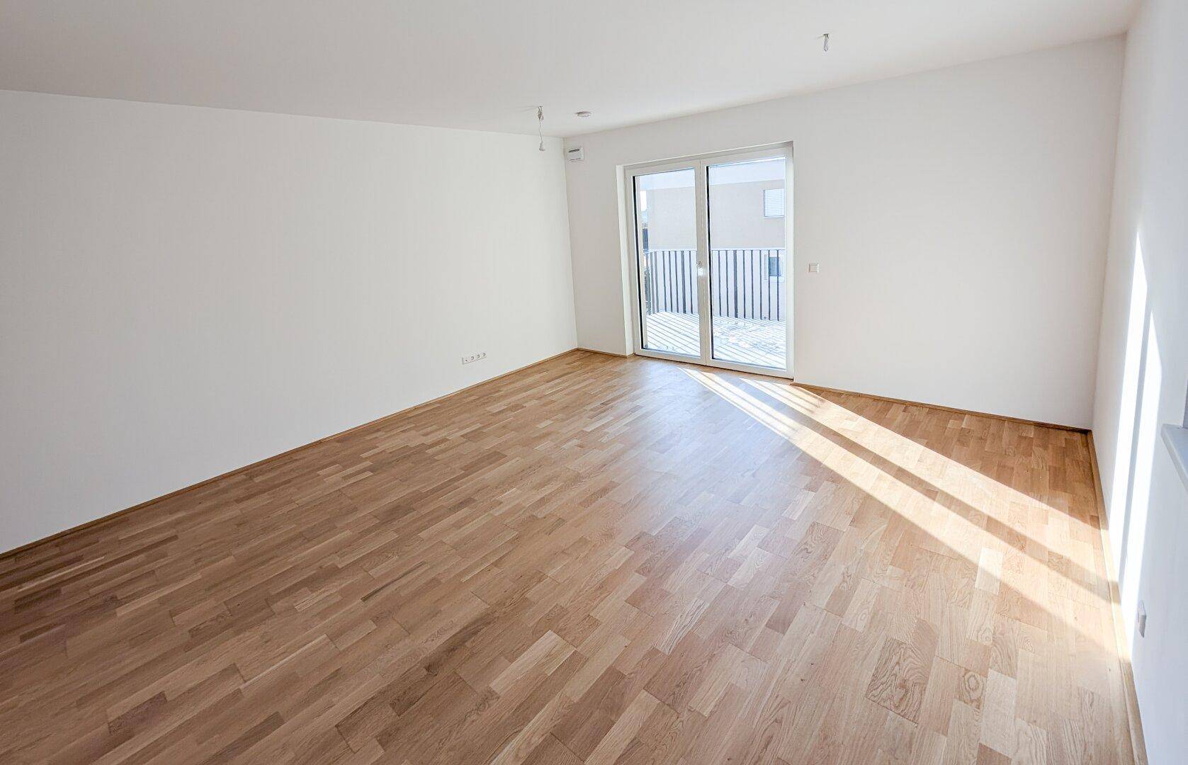 Heller, moderner Raum mit Parkettboden, großen Fenstern und direktem Zugang zu einem Balkon.