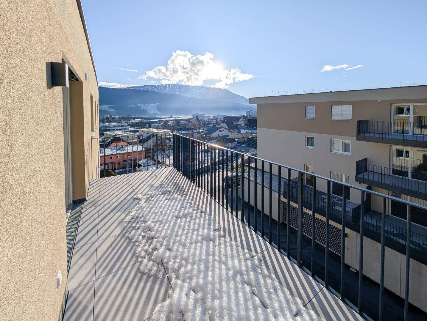 Sonnenverwöhnter Balkon mit Bergblick über die Stadt, teilweise mit Schnee bedeckt.