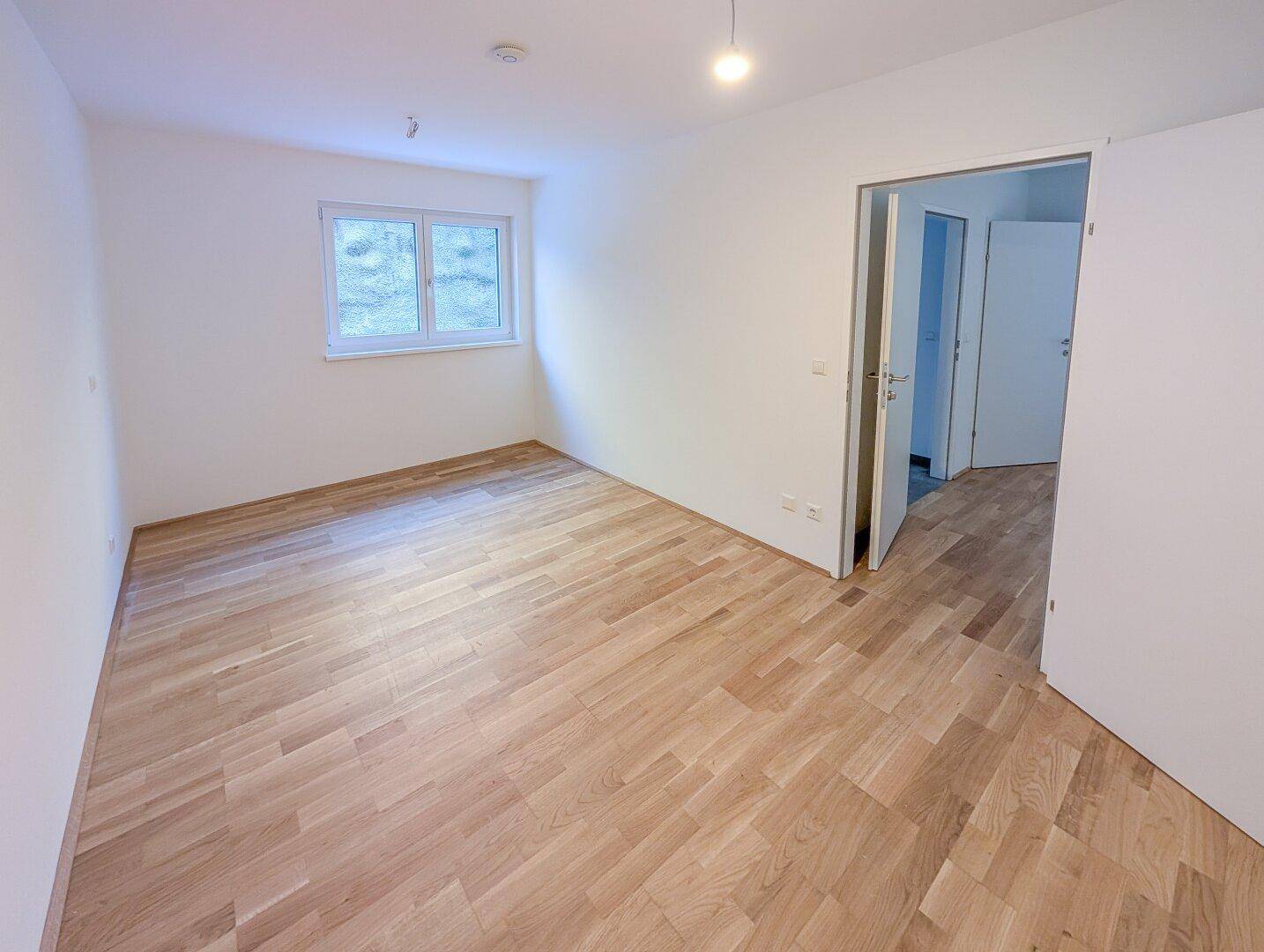 Geräumiges Schlafzimmer mit hellem Parkettboden und großem Fenster.