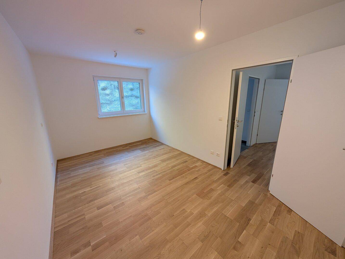 Helles, leeres Zimmer mit Holzparkettboden und einem Fenster, bereit zur individuellen Gestaltung.