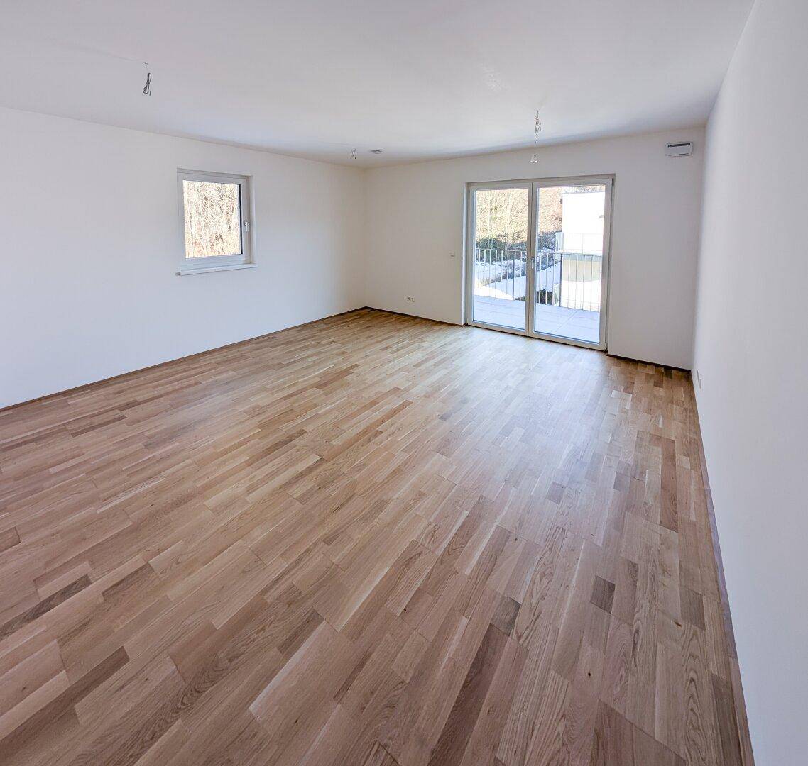 Großes, helles Wohnzimmer mit Holzboden und Zugang zu einem Balkon, ideal für offenes Wohnen.