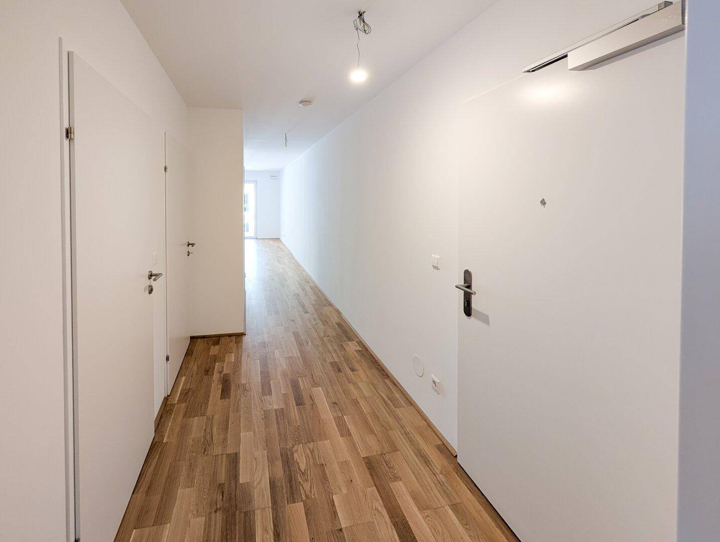 Langer, heller Flur mit Holzboden und mehreren Türen zu den angrenzenden Räumen.