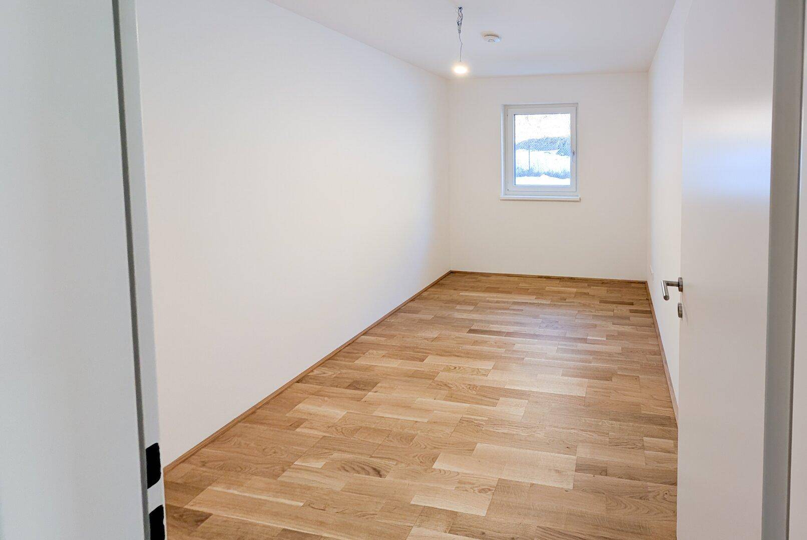 Helles, leeres Zimmer mit Holzboden und einem Fenster, ideal als Schlaf- oder Arbeitszimmer.