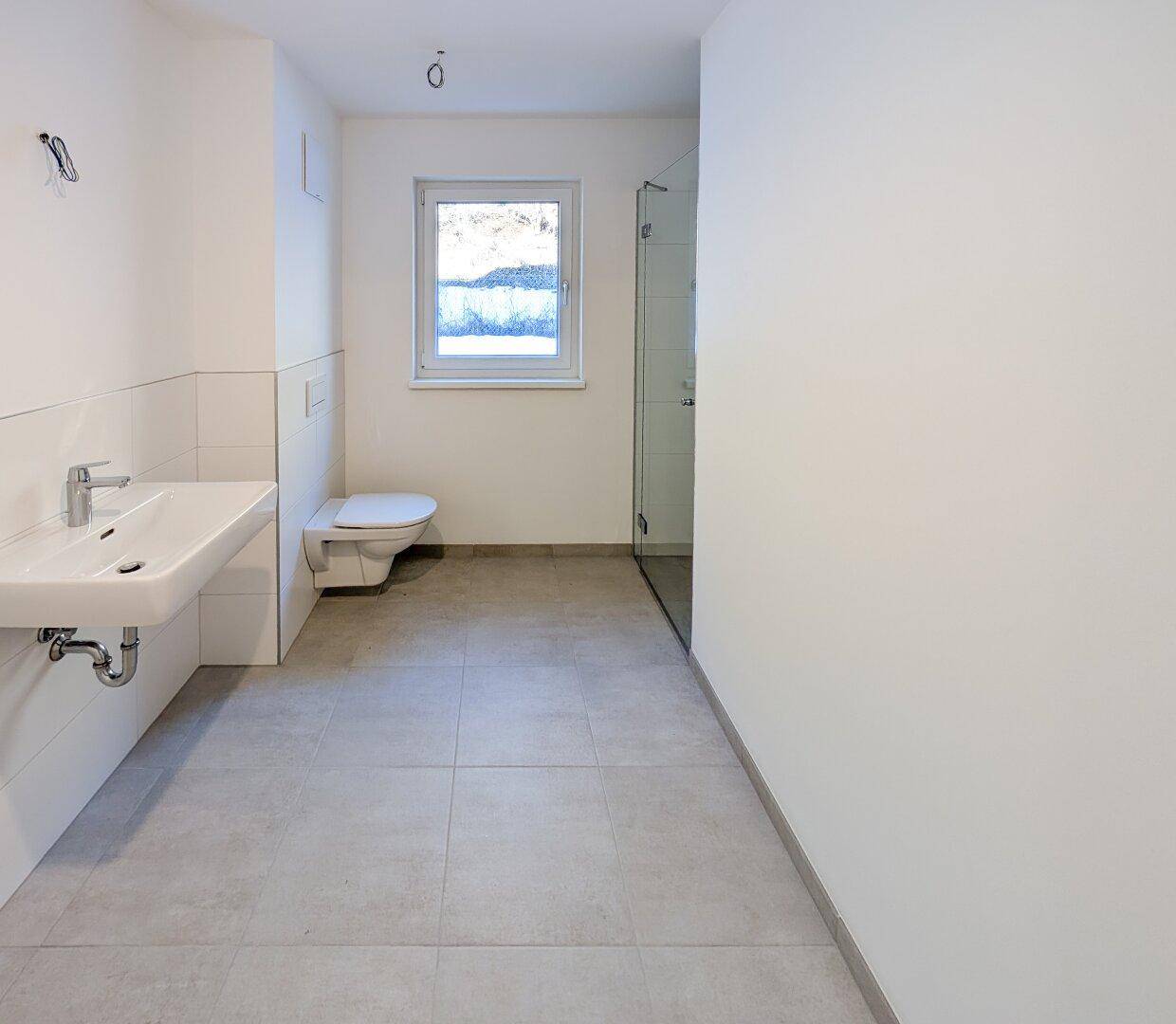 Modernes Badezimmer mit großformatigen Fliesen, wandhängendem WC und ebenerdiger Dusche.