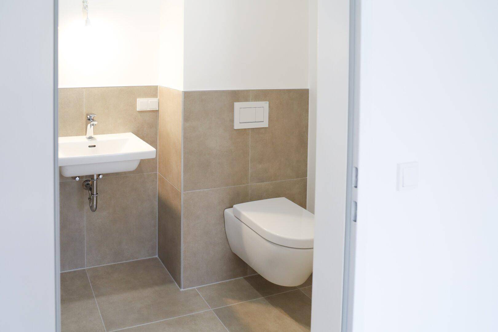 Kompaktes Gäste-WC mit wandhängender Toilette, modernem Waschbecken und Fliesenboden.