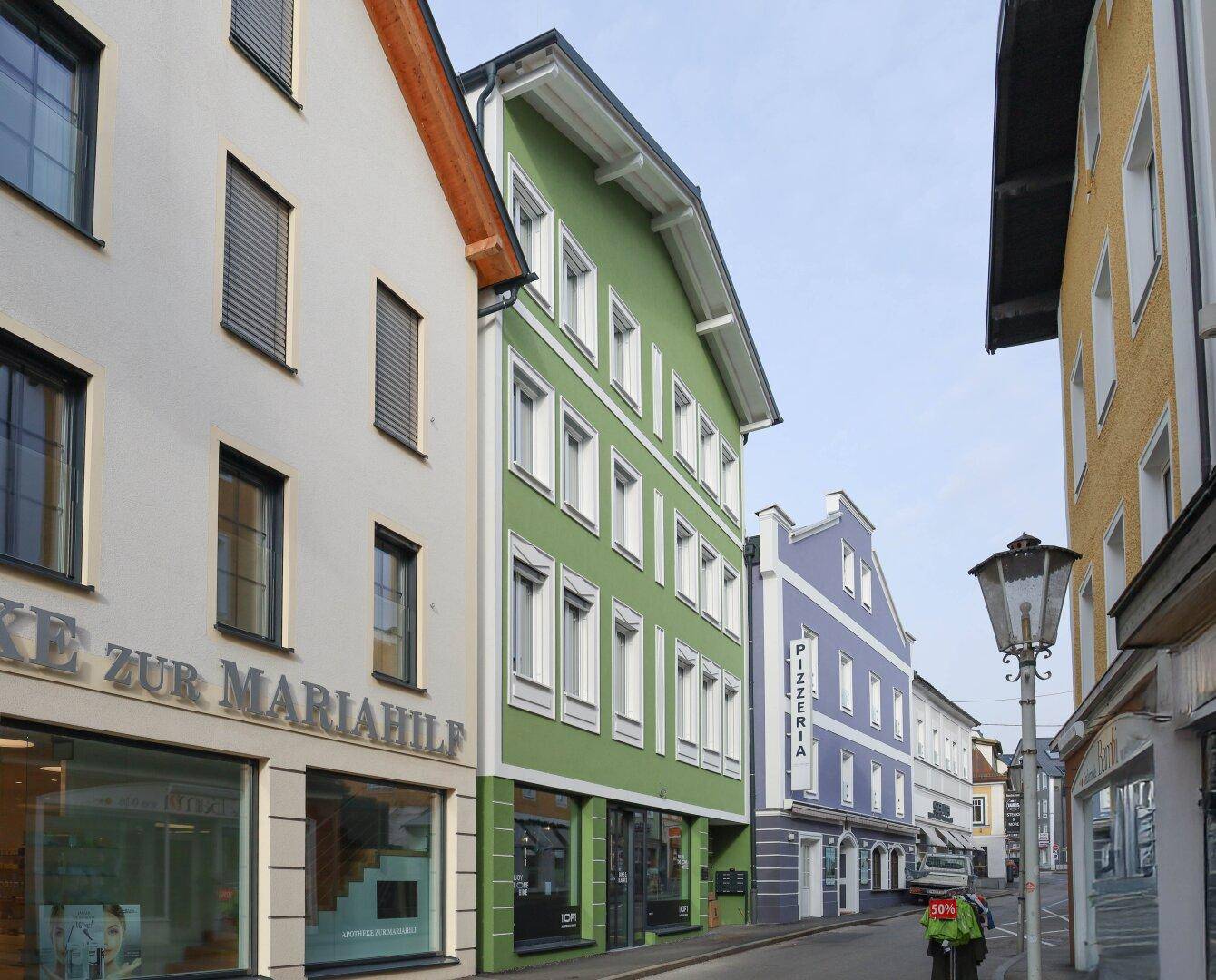 Blick auf eine belebte Straße mit farbenfrohen Gebäudefassaden und Geschäften im Erdgeschoss.
