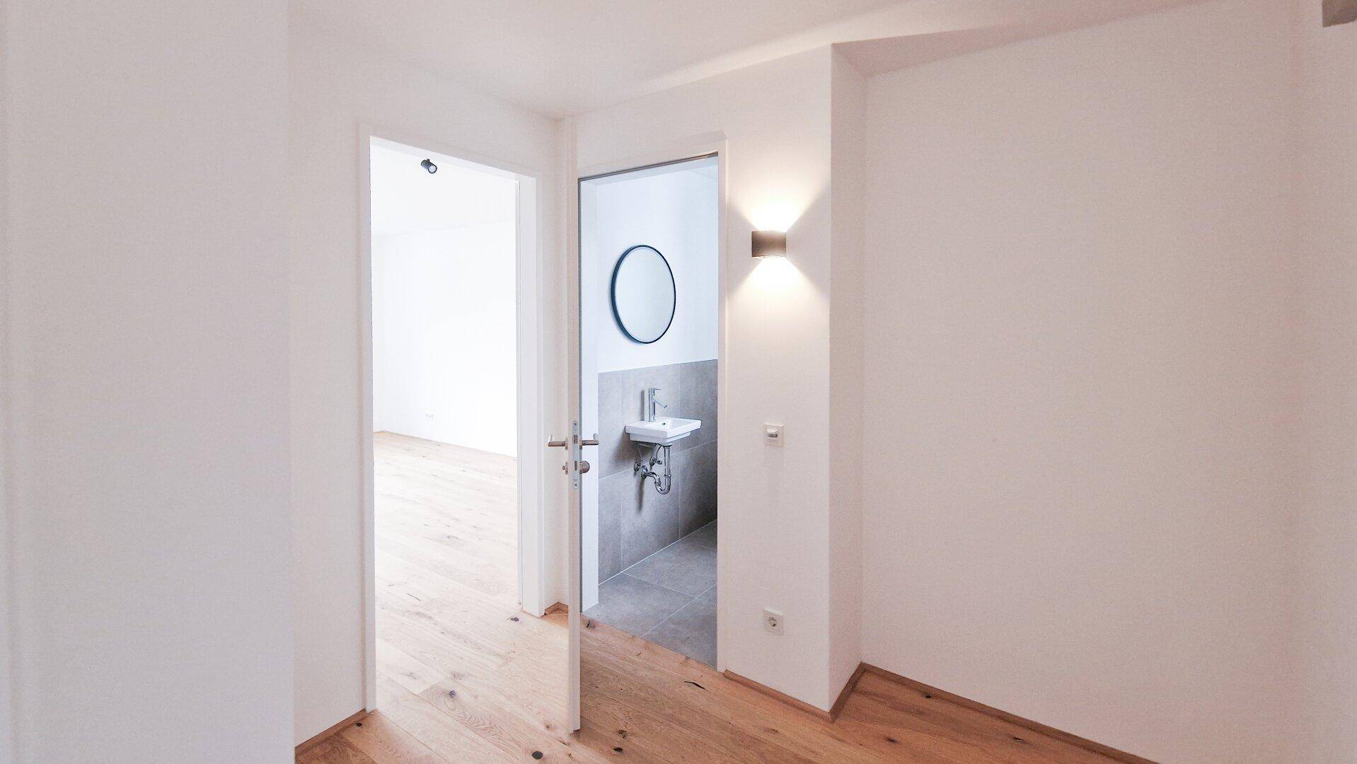 Heller Flur mit Holzboden und Zugang zu einem modernen Badezimmer mit Waschbecken.
