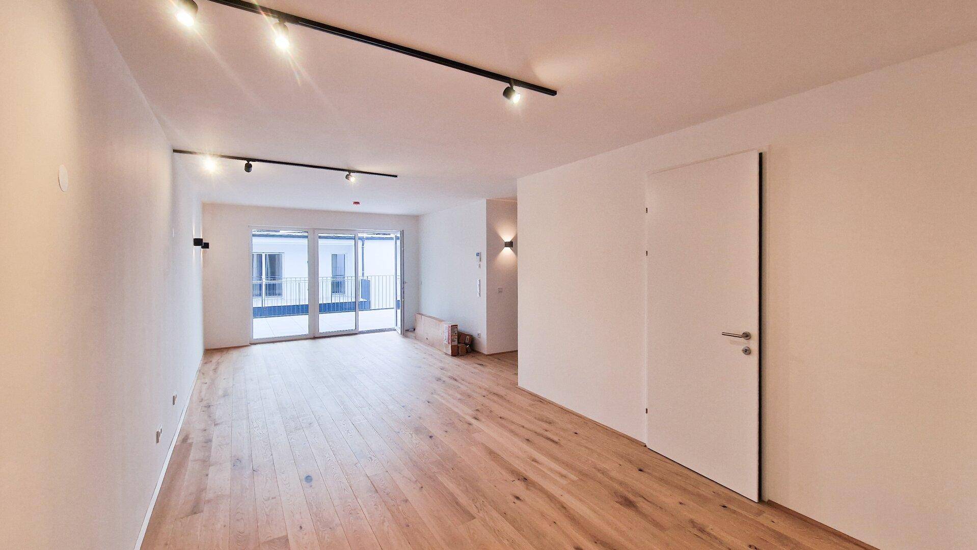 Lichtdurchfluteter Wohnbereich mit Holzboden, moderner Beleuchtung und großzügigem Terrassenzugang.