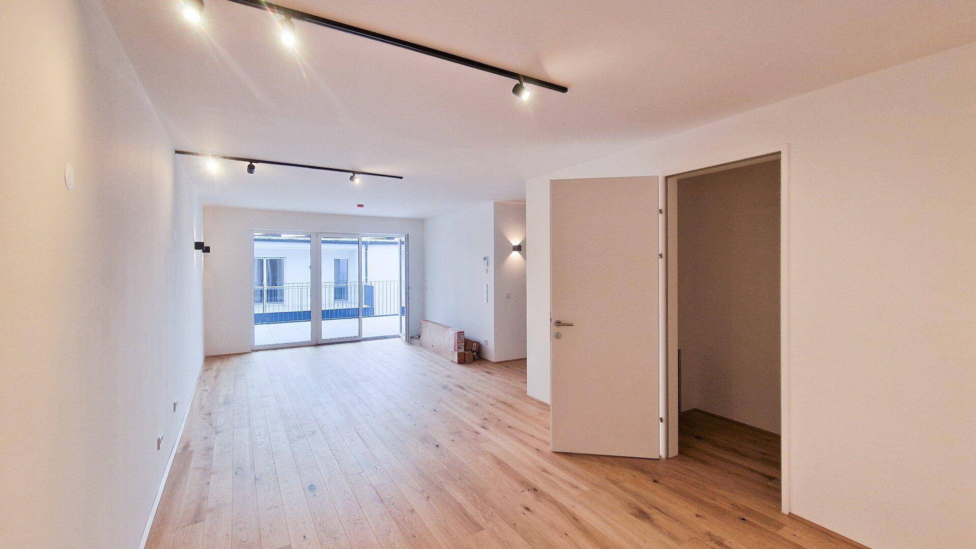 Heller Wohnraum mit Holzboden, Schiebetür zur Terrasse und offenem Zugang zu einem Abstellraum.