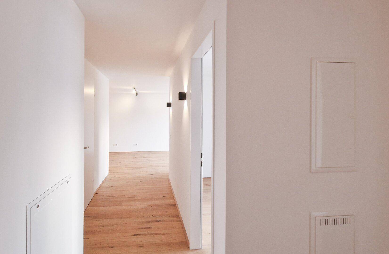 Langer, heller Flur mit Holzboden und integrierten Wandpaneelen, der zu weiteren Räumen führt.