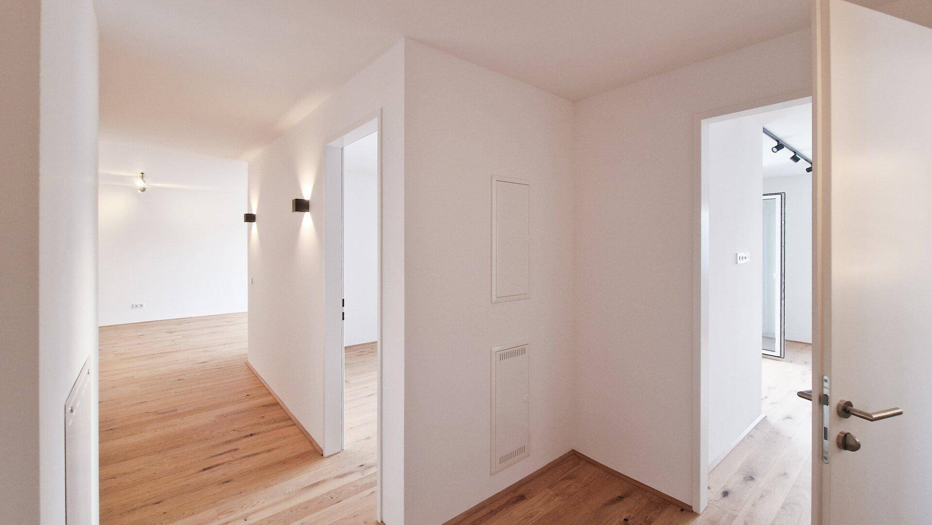 Heller Flurbereich mit Holzboden, mehreren Türen und modernen Wandleuchten, die den Raum erhellen.