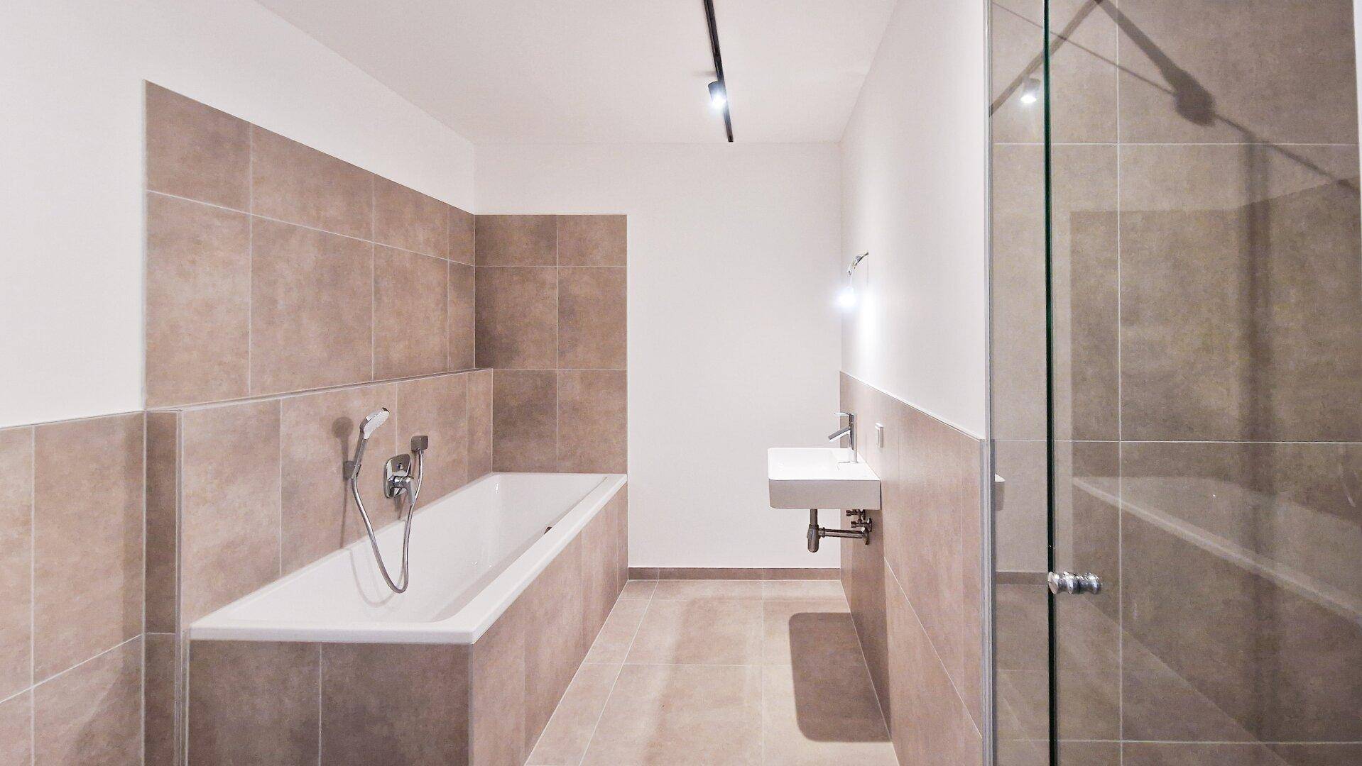 Modernes Badezimmer mit Badewanne, schwebendem Waschbecken und großformatigen Fliesen an Wänden und Boden.