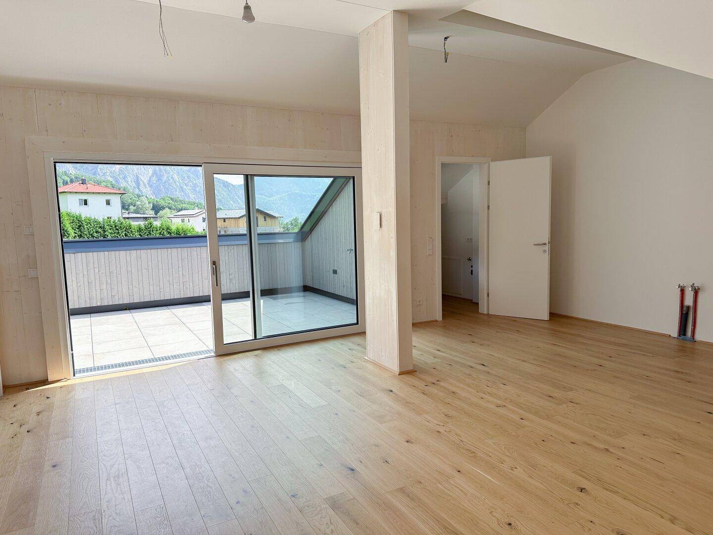 Heller Wohnraum mit Holzboden, großen Schiebetüren zur Terrasse und Bergblick.