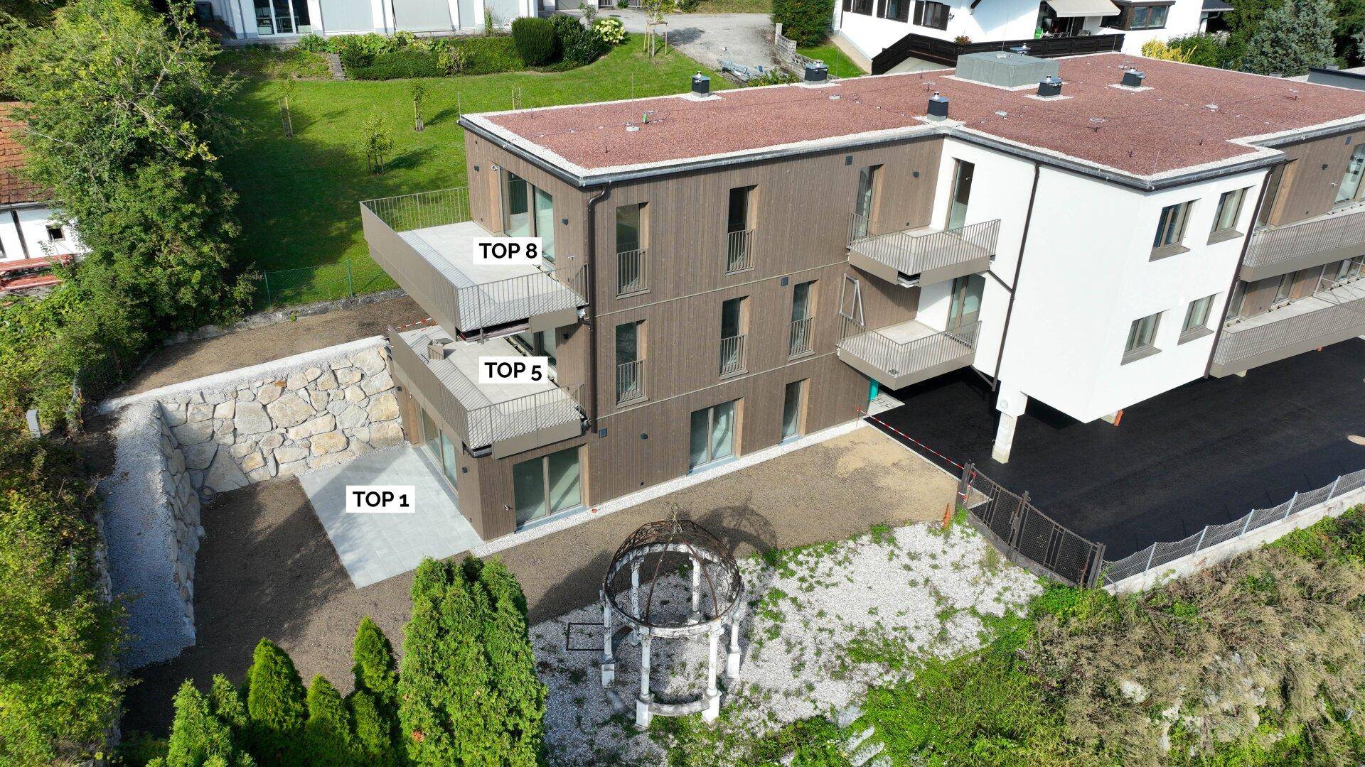 Moderne Wohnanlage mit Holzfassade, Flachdach und mehreren Balkonen, umgeben von Grünflächen.