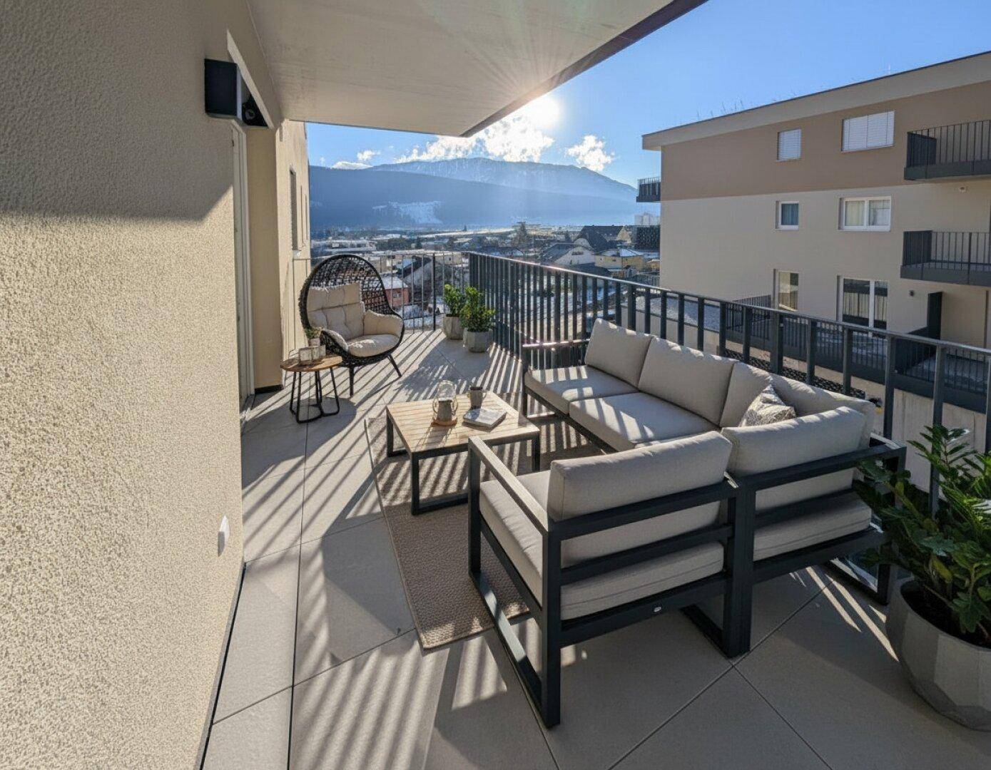 Sonniger Balkon mit modernen Outdoor-Möbeln und einem weiten Blick auf die umliegende Berglandschaft.