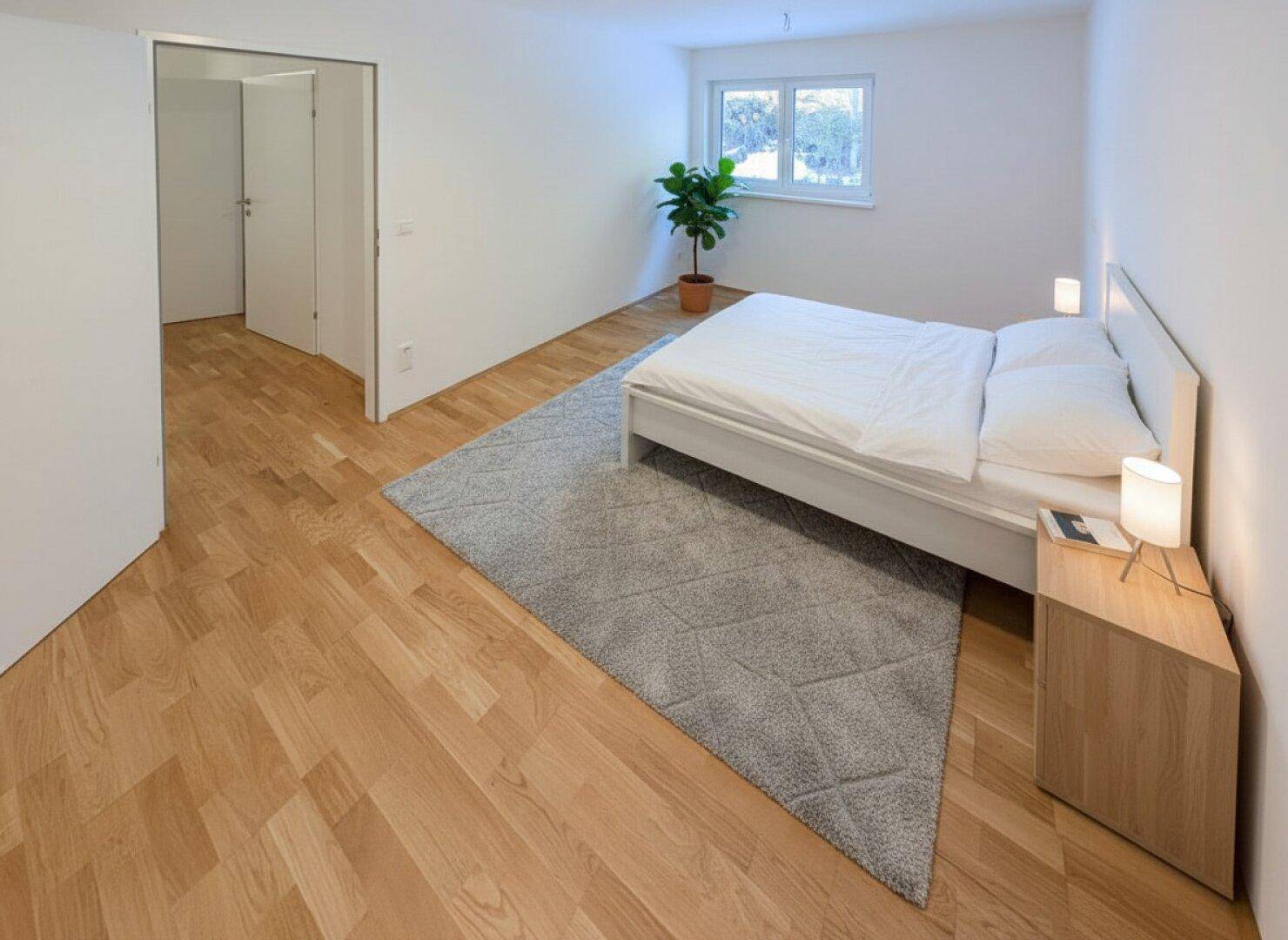Helles Schlafzimmer mit modernem Holzboden, einem bequemen Bett und einem Fenster mit Grünblick.