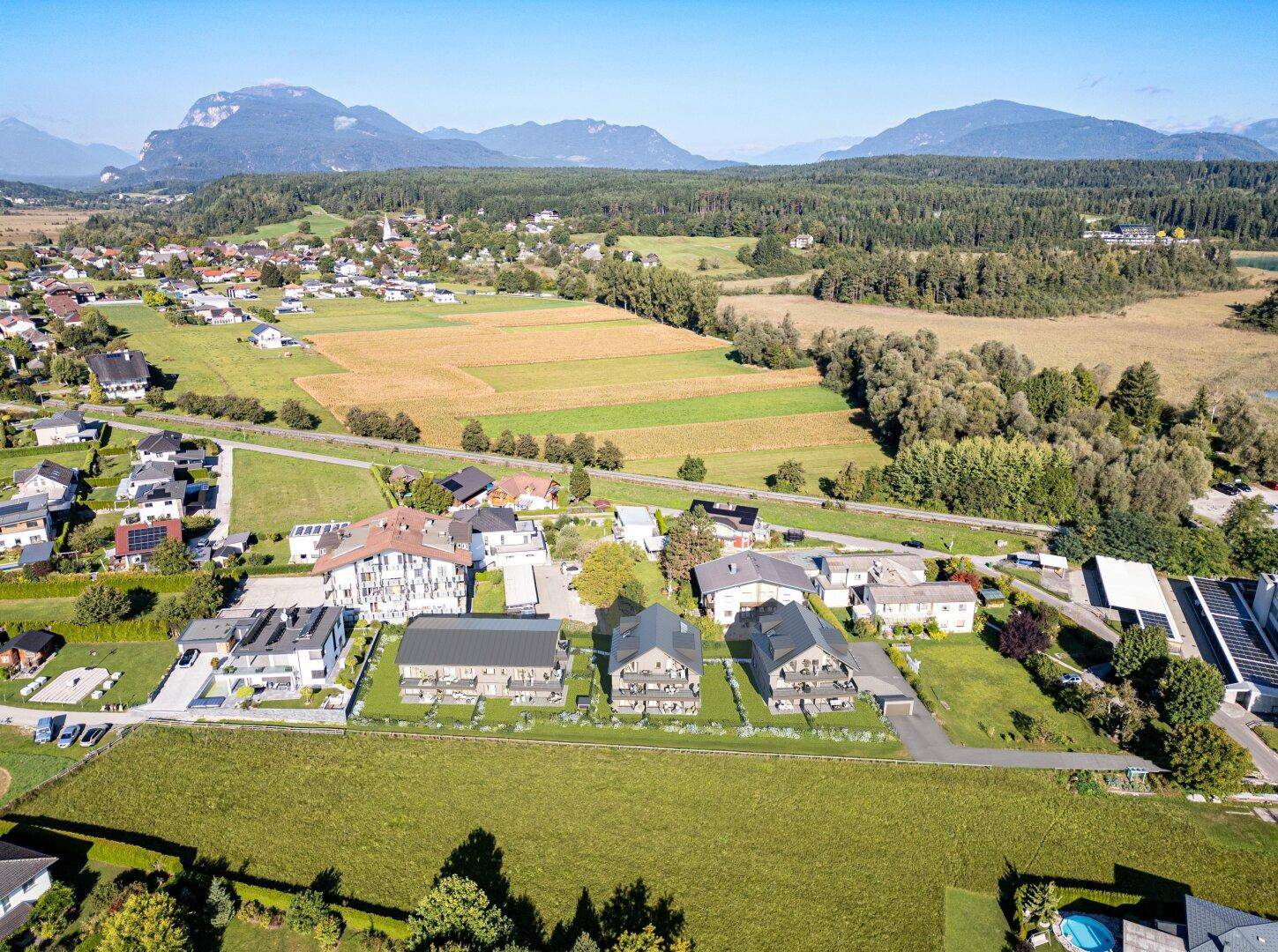 Weitläufige Luftaufnahme einer Wohnsiedlung eingebettet in grüne Felder mit Bergen im Hintergrund.