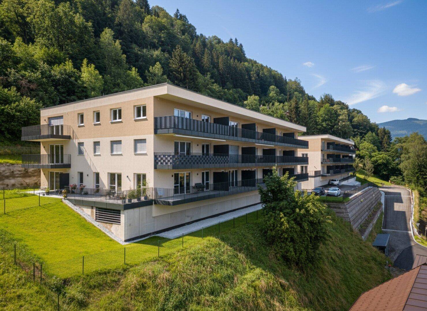 Neubau-Wohngebäude mit modernen Balkonen und Blick auf die bewaldeten Hügel.