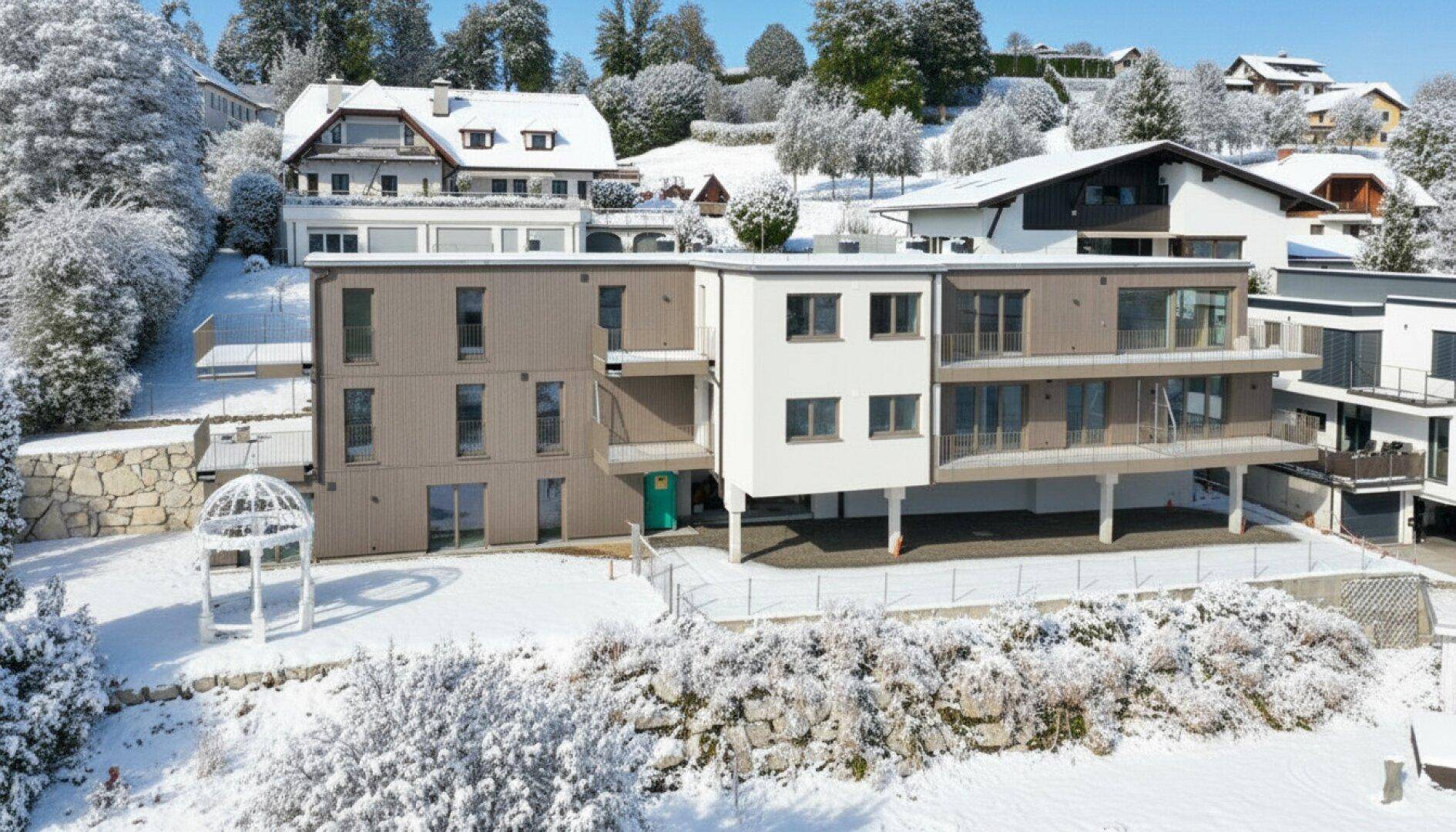 Modernes Apartmentgebäude im Winter mit schneebedeckter Umgebung und Balkonen.