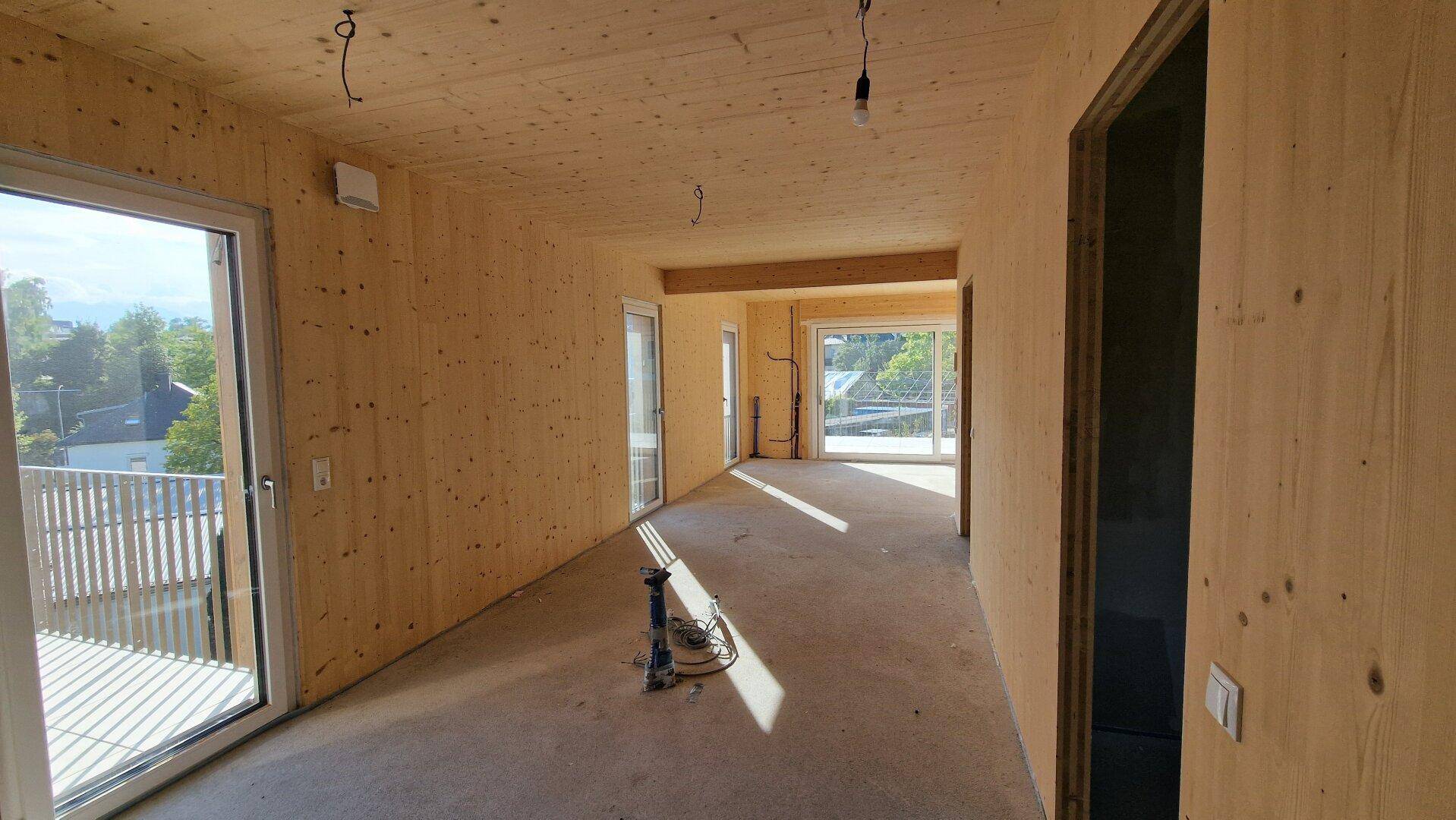 Unfertiger Innenraum mit Holzverkleidung an Wänden und Decken sowie großen Fenstern.