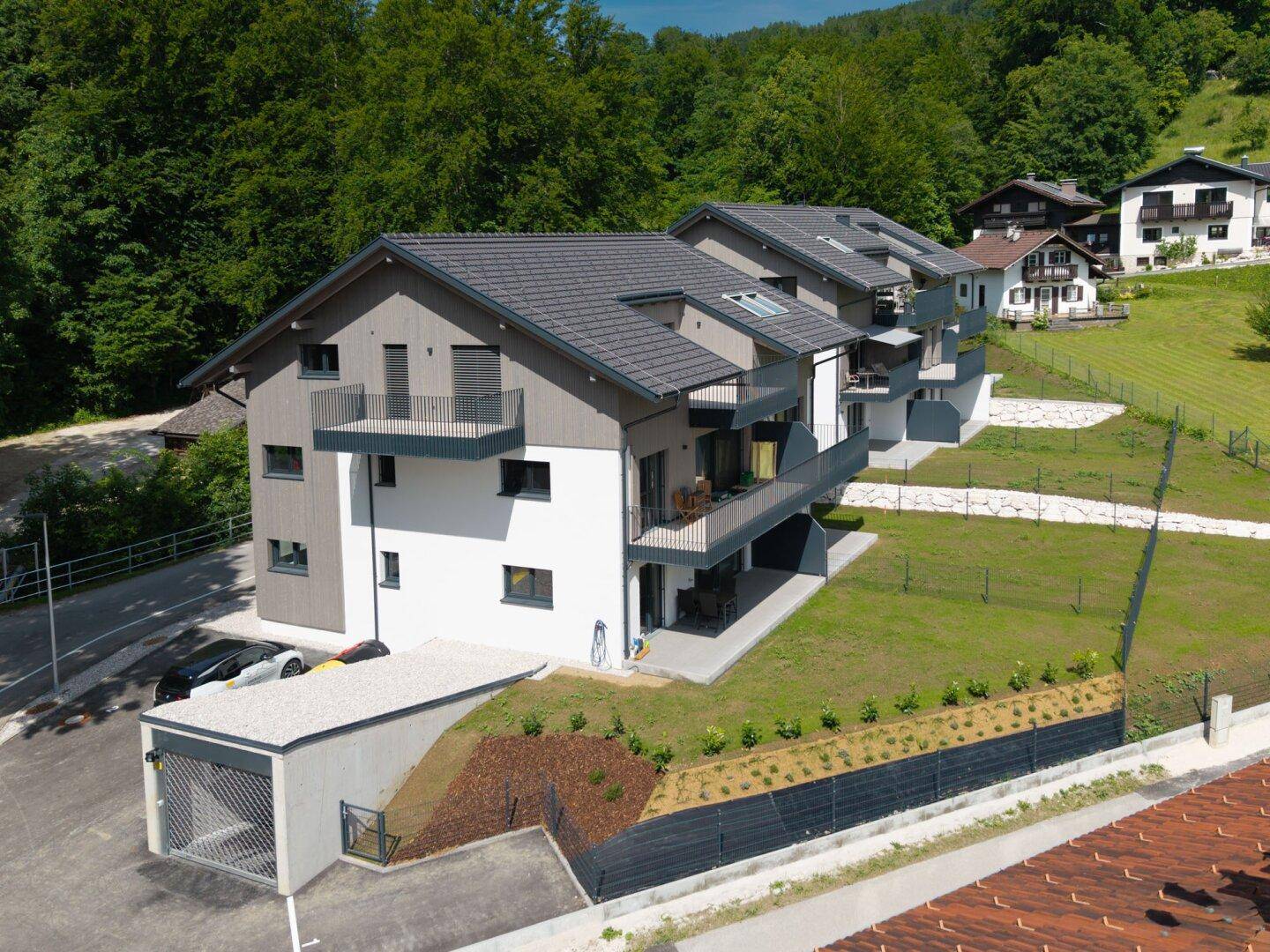 Modernes Mehrfamilienhaus mit Balkonen und integrierter Tiefgarage in einer grünen Umgebung.