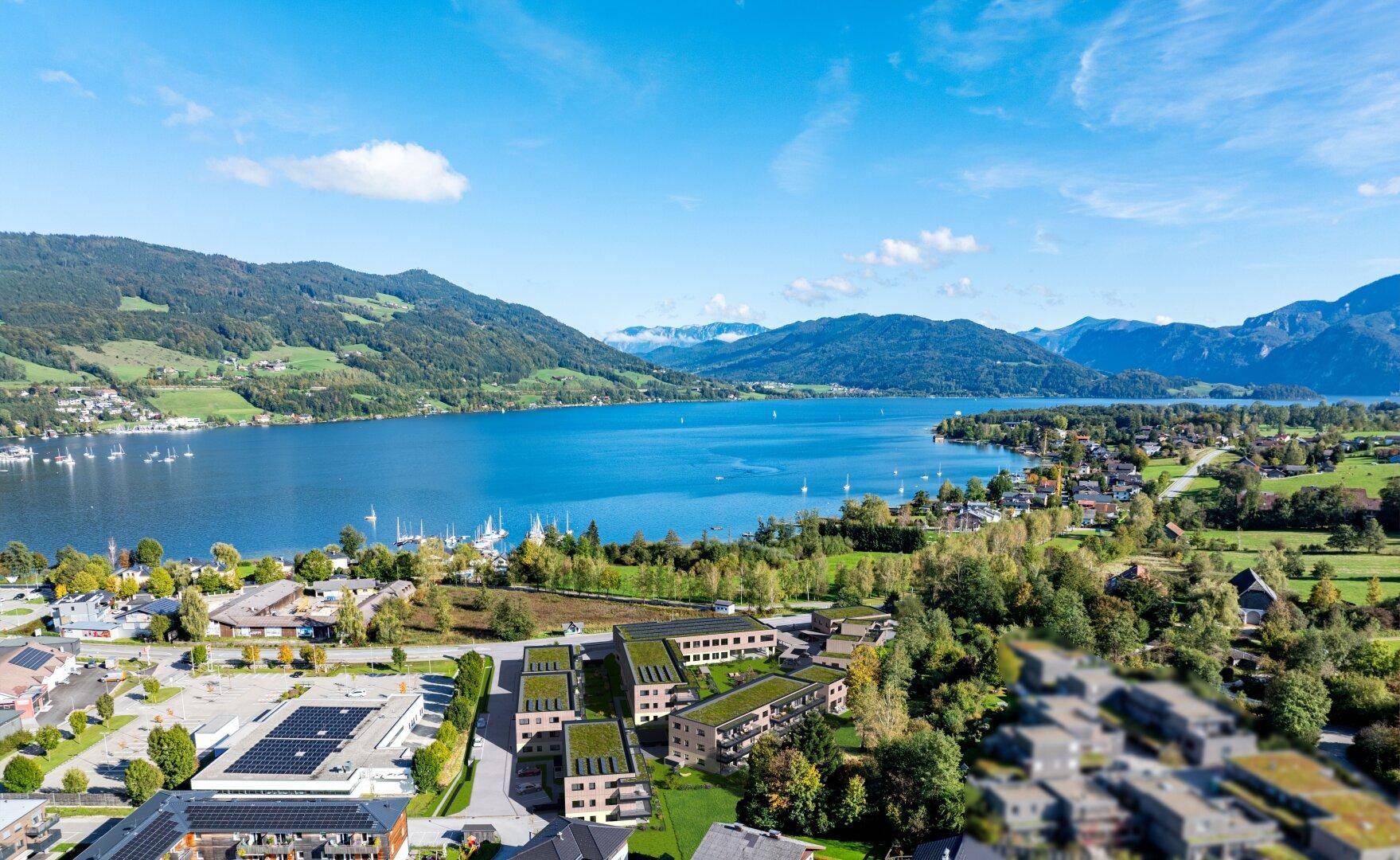Luftaufnahme einer Wohnanlage am Seeufer mit Bergblick und grüner Umgebung.