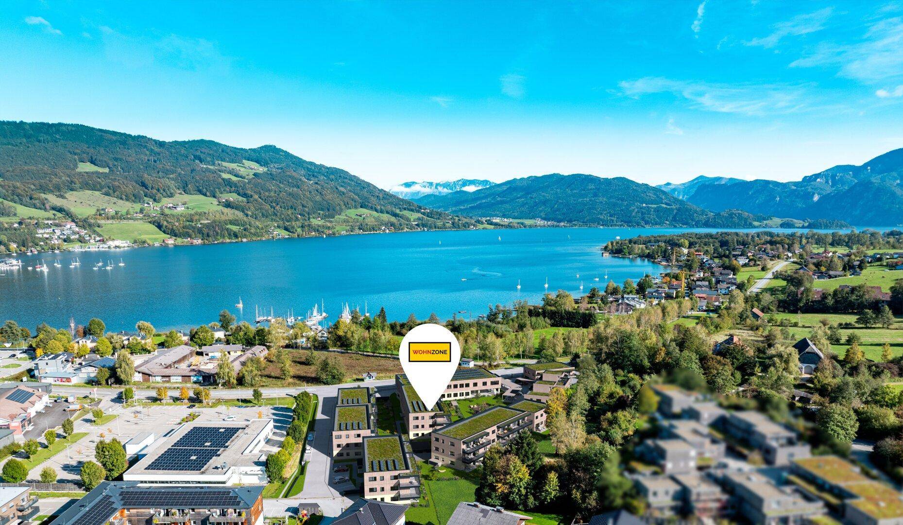 Luftaufnahme eines modernen Wohnkomplexes mit Seeblick und umgeben von grünen Bergen.