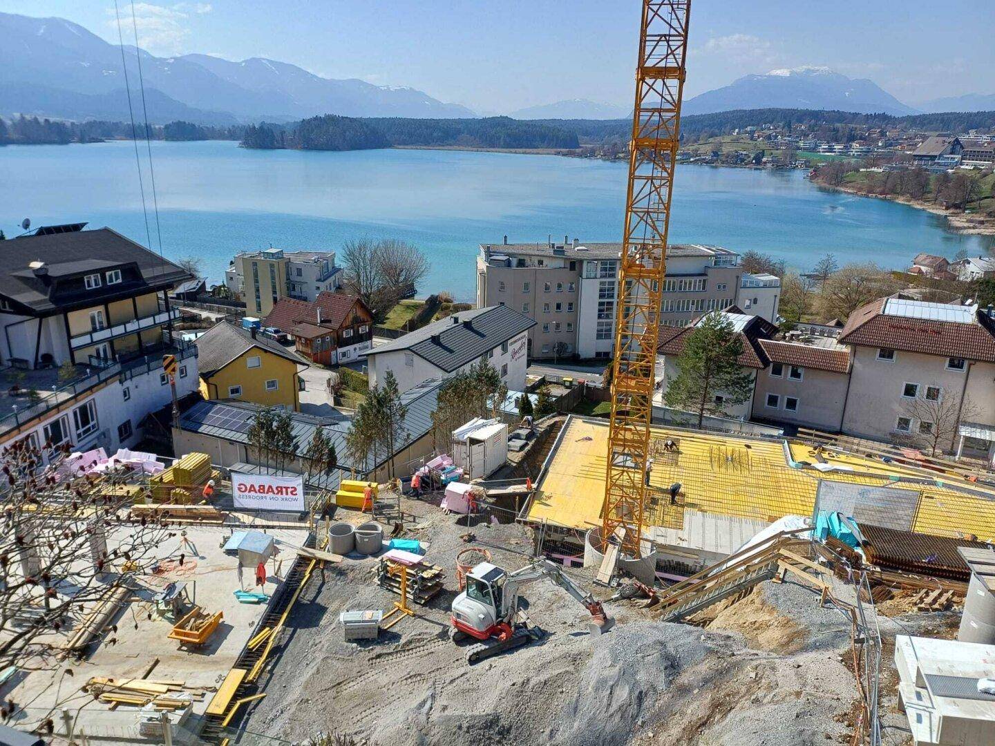 Baustelle eines Neubaus mit Kran und Blick auf den Faaker See und die umliegenden Berge.