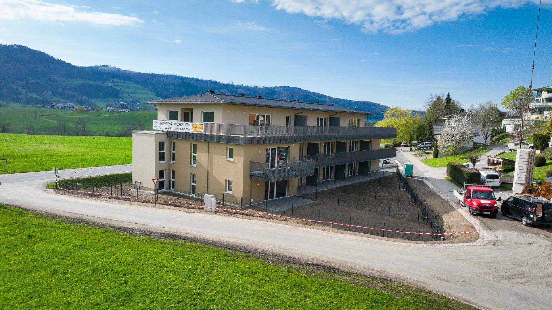Modernes Neubau-Mehrfamilienhaus mit Balkonen und Blick auf die umliegende Natur und Berge.