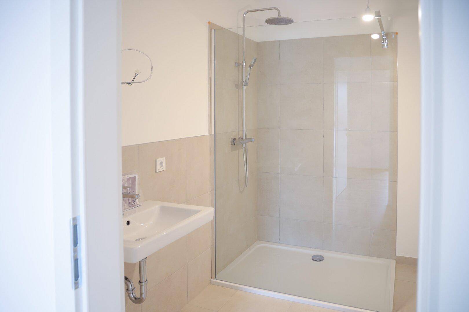 Modernes Badezimmer mit ebenerdiger Dusche, einzelnen Waschbecken und hellen Fliesen.