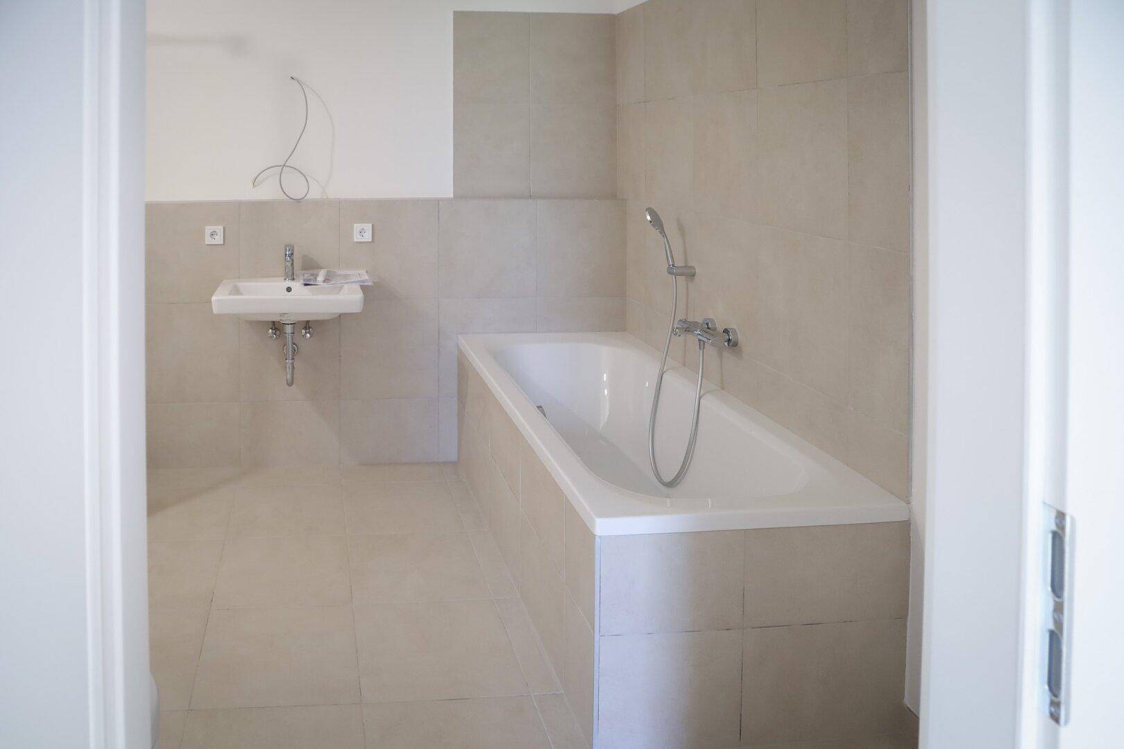 Modernes Badezimmer mit Badewanne, Waschbecken und hellen Fliesen an Wänden und Boden.