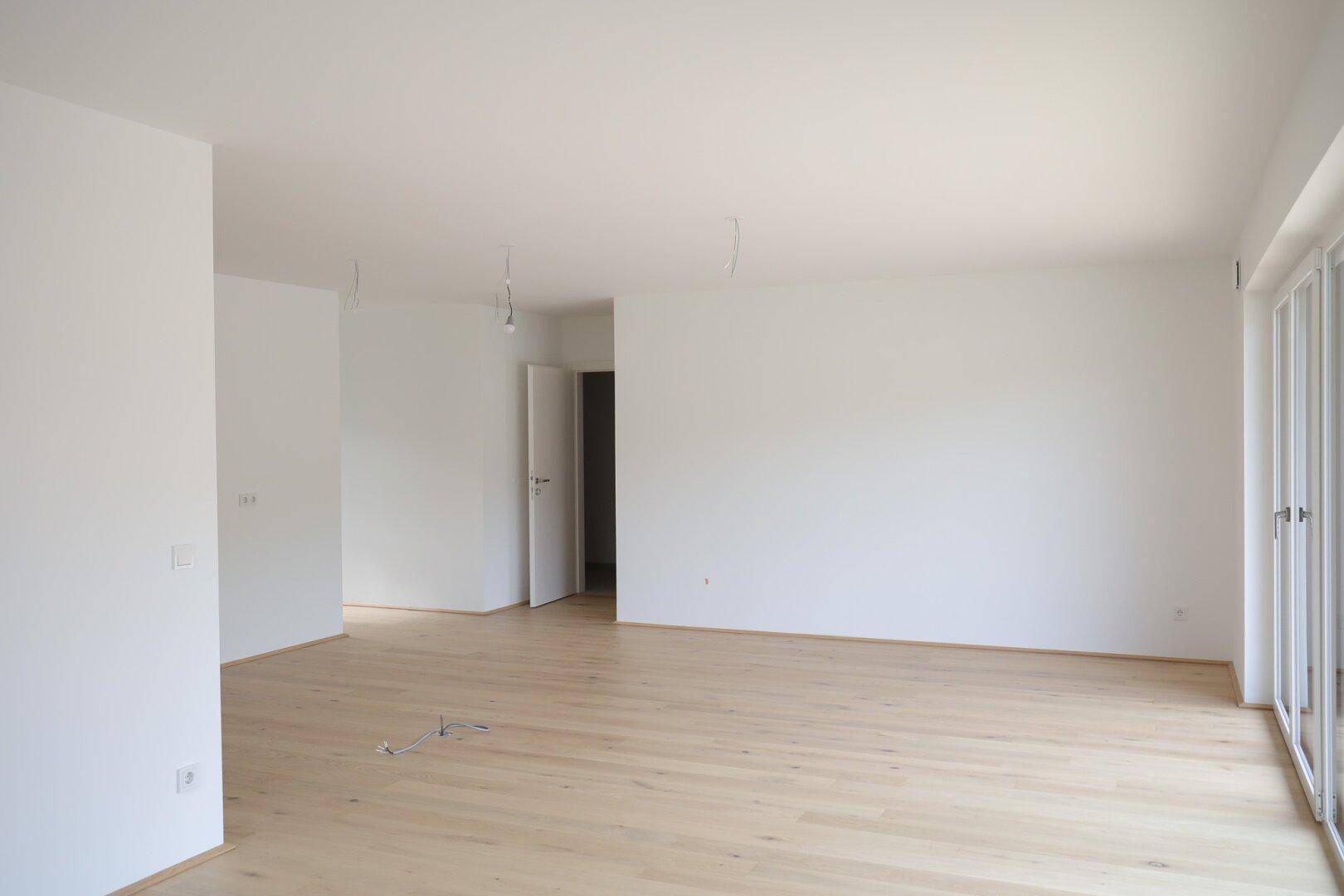 Heller, leerer Wohnraum mit neuem Parkettboden und direktem Zugang zur Terrasse.