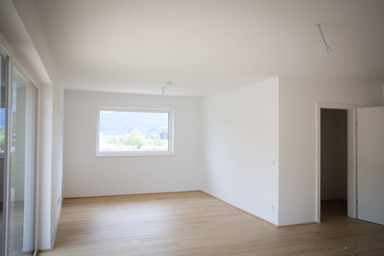 Geräumiger Wohnraum mit großen Fenstern und weitem Blick in die grüne Natur.