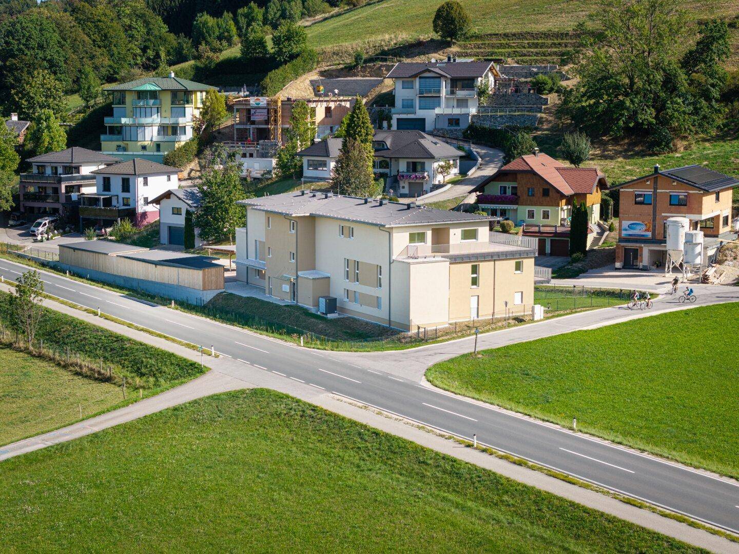 Neues Wohngebäude in einer Siedlung, umgeben von weiteren Häusern und grüner Landschaft.